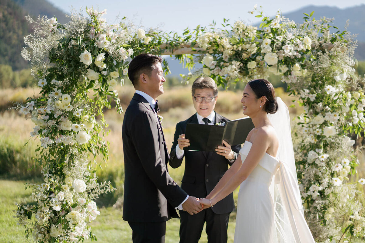 Bride and Groom stand at the altar surrounded by a bountiful wedding flower arch at their Aspen Meadows Resort wedding ceremony.