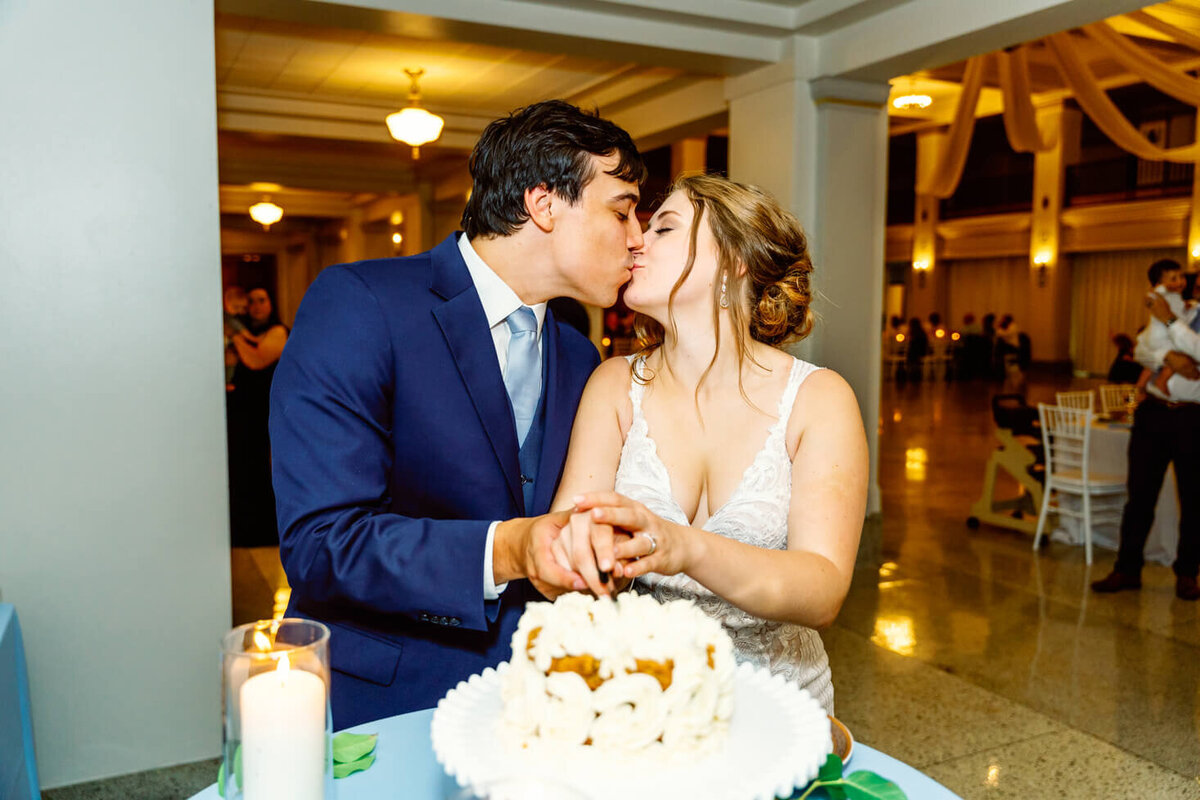Bride and groom sharing a kiss while cutting their wedding cake.