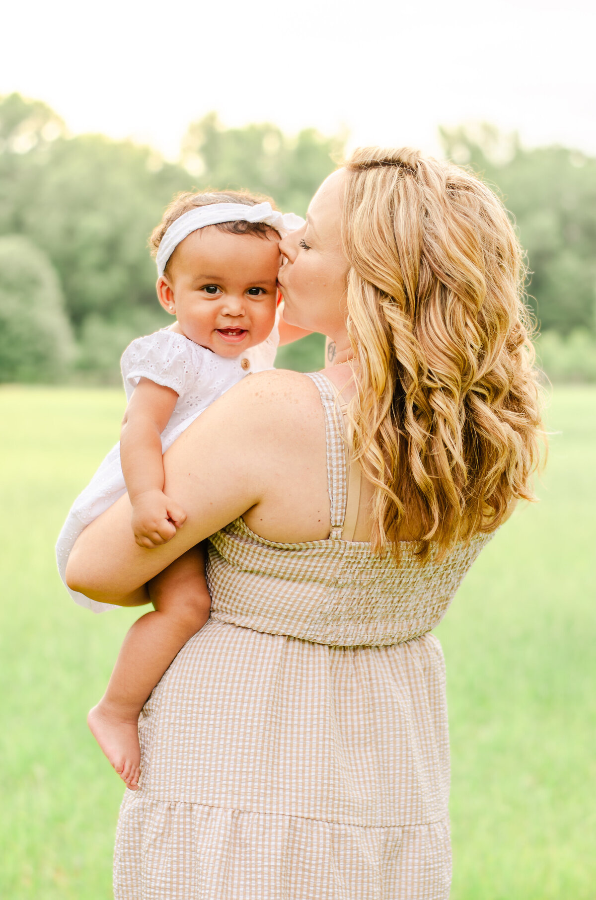 mom kisses baby in a field