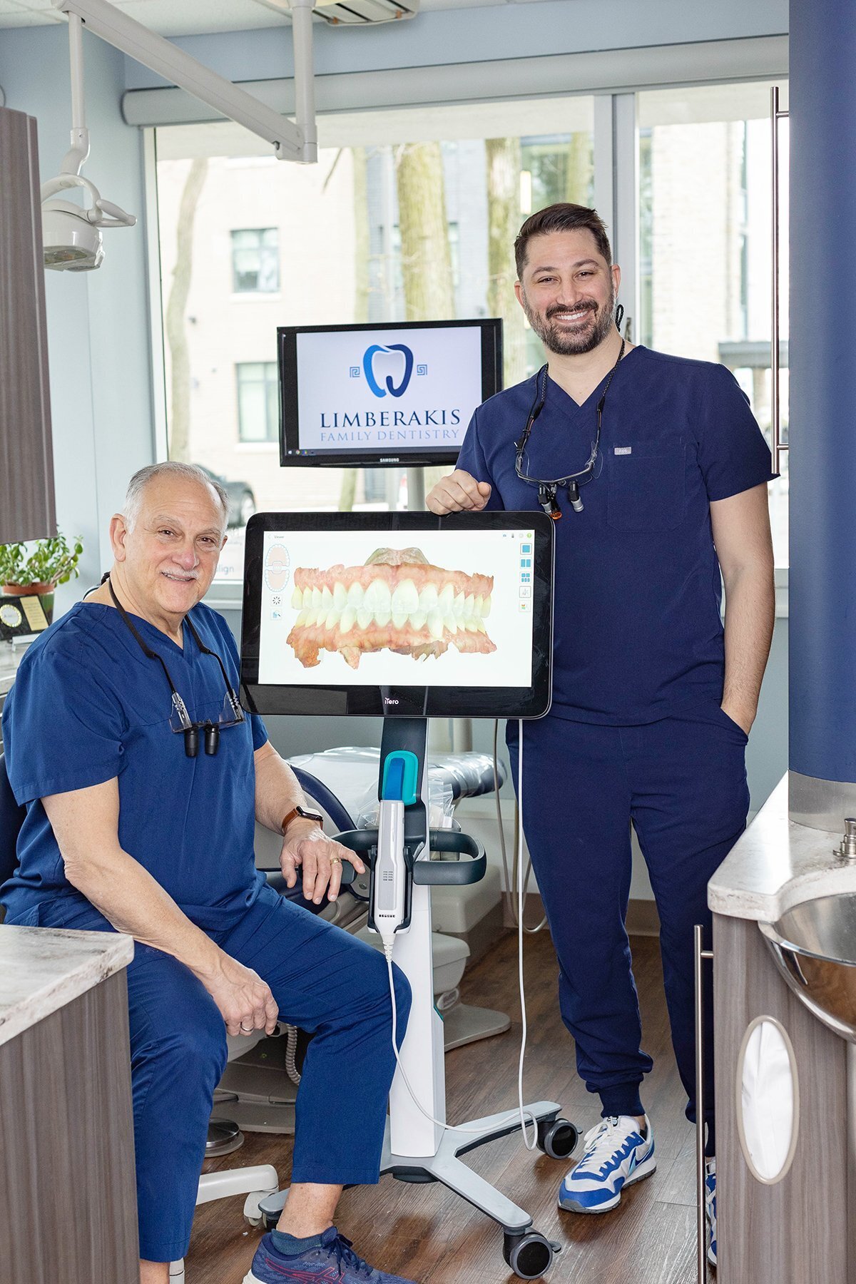 Two dentists in a dental exam room smiling at the camera
