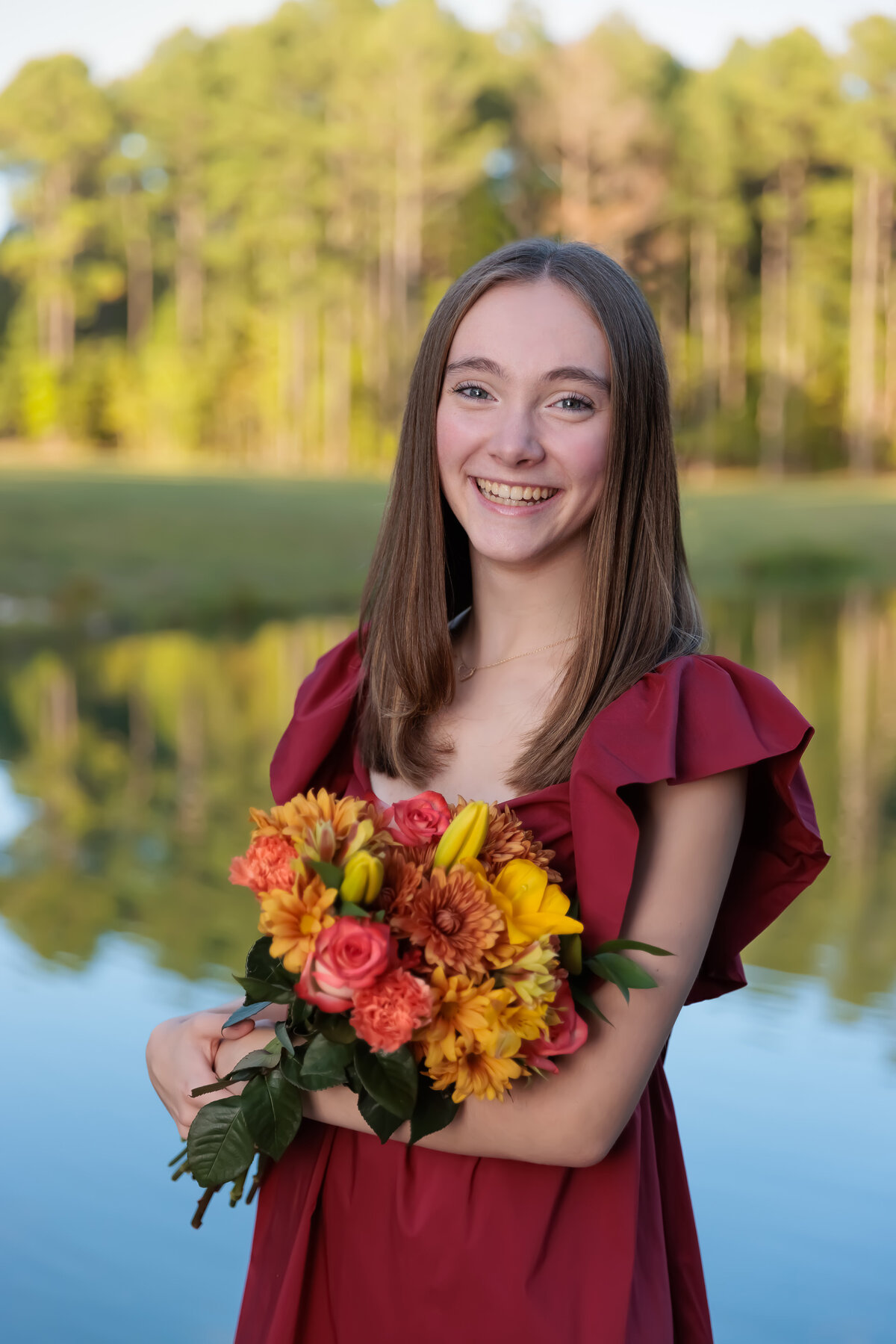 Teen Portraits in the fall holding flowers by a pond in Apex, NC.
