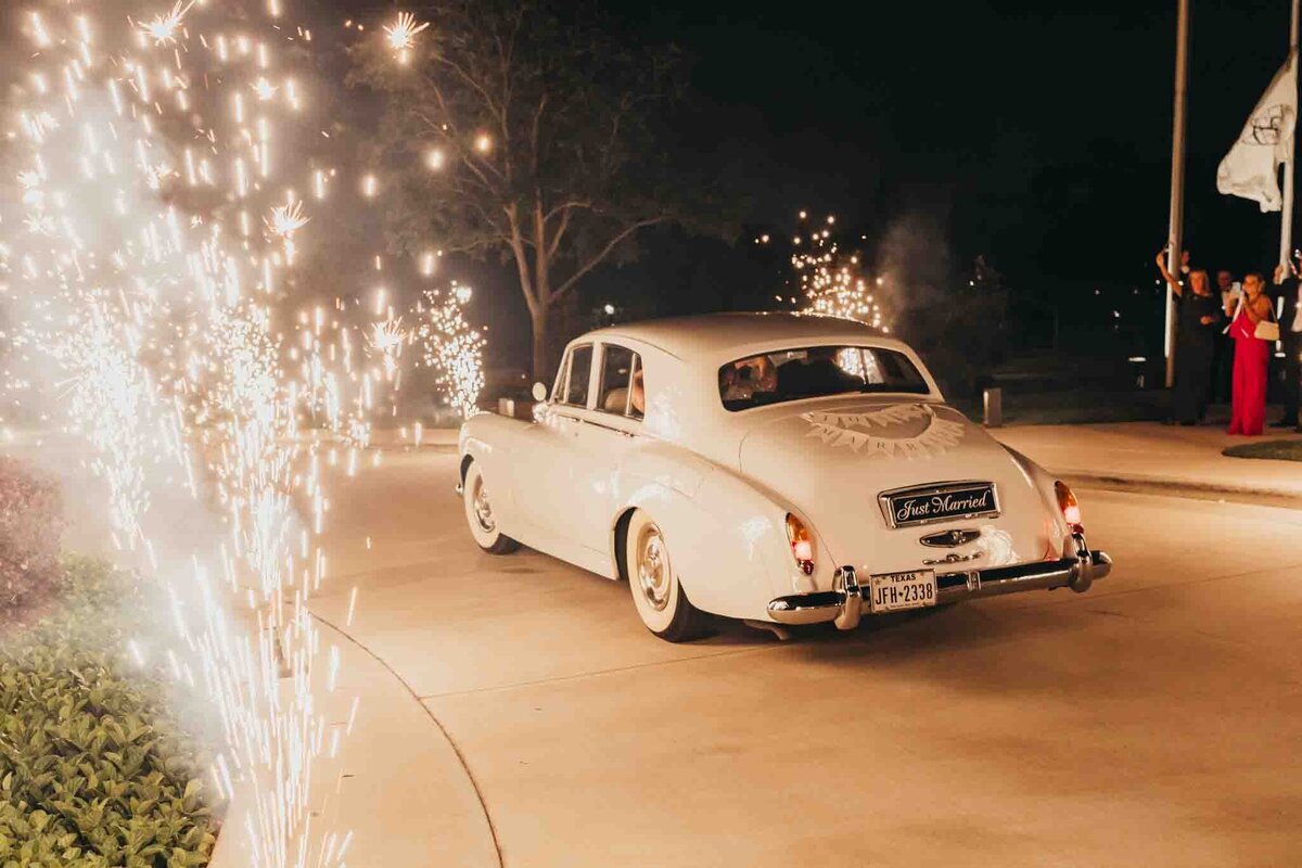 getaway car is an old rolls royce, for bride and groom and is lit by fireworks along the driveway at night.