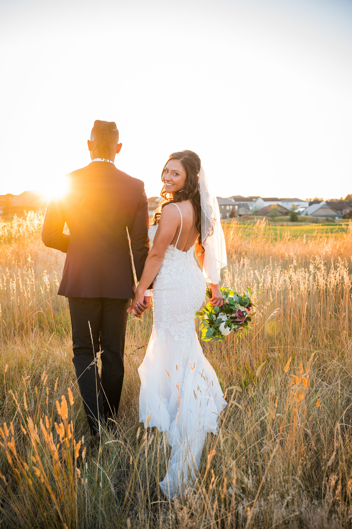 A bride holds hands with her groom and glances over her shoulder at golden hour.