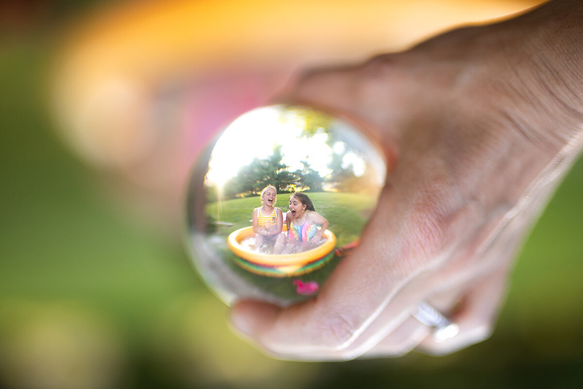 girls playing in little pool seen through glass ball