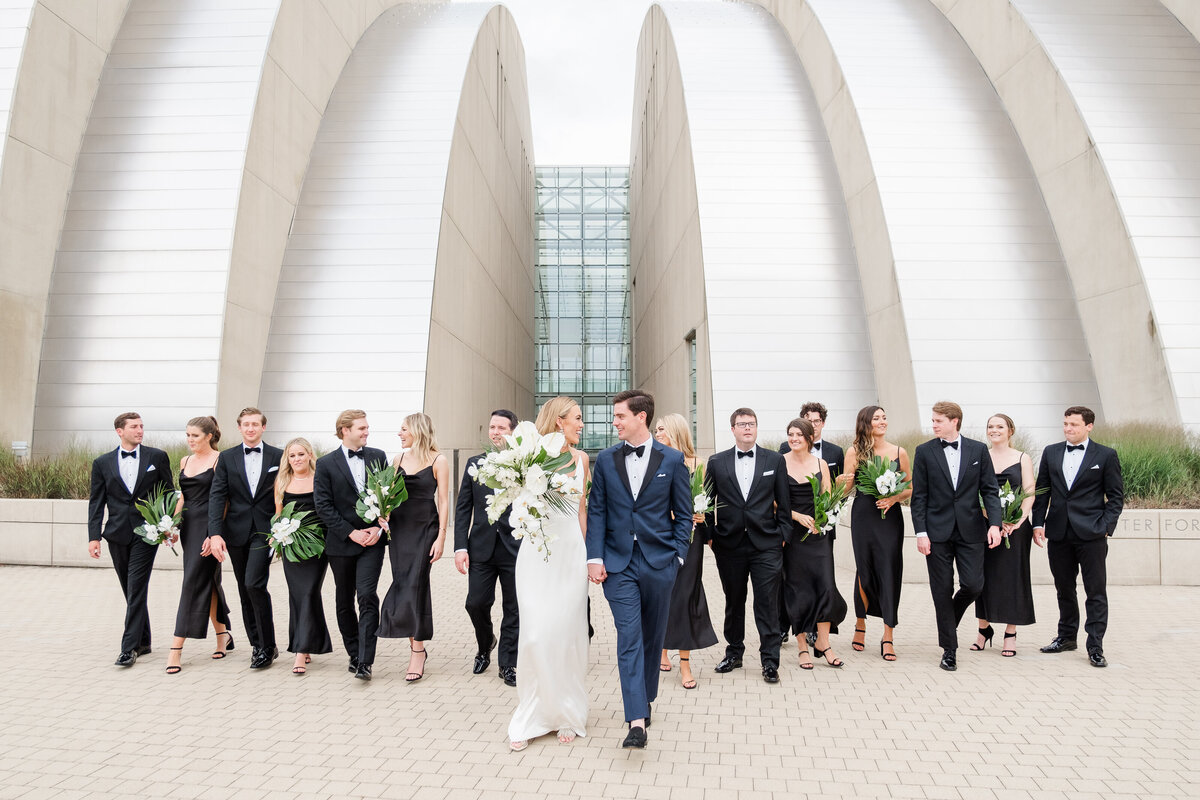 black tie and black BHLDN bridesmaids wedding party walking in front of Kauffman Center with bride and groom