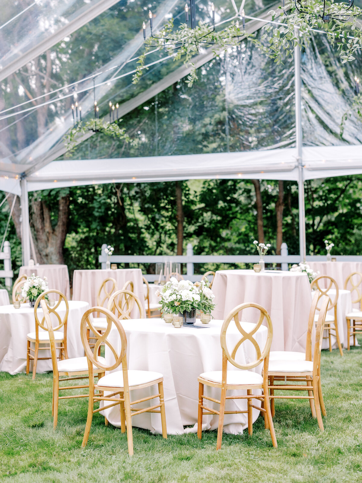Reception tables with wood chairs and floral centerpieces under a clear tent
