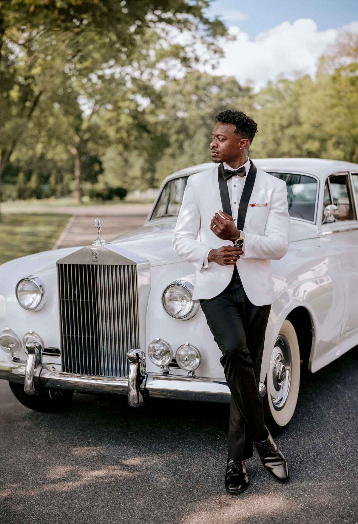 groom-in-white-tuxedo-leaning-on-rolls-royce