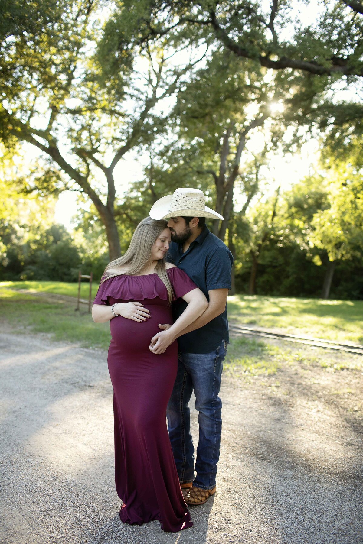 A romantic maternity photo of the expectant mom and dad snuggling together in the park, sharing a tender moment as they smile and embrace, captured by Chunky Monkey Photography.