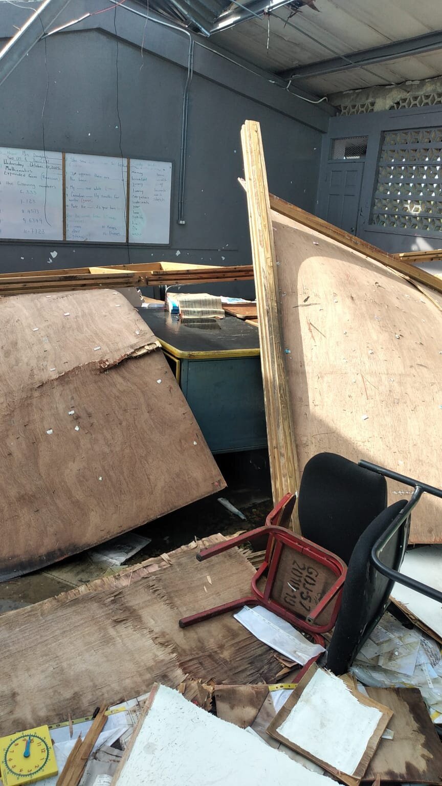 Water-damaged furniture and a collapsed wall panel lying on the classroom floor.