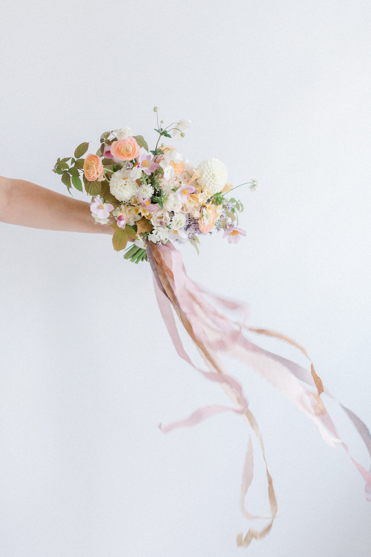 A hand holds a bouquet of pastel flowers with a long pink ribbon in a Montreal studio.