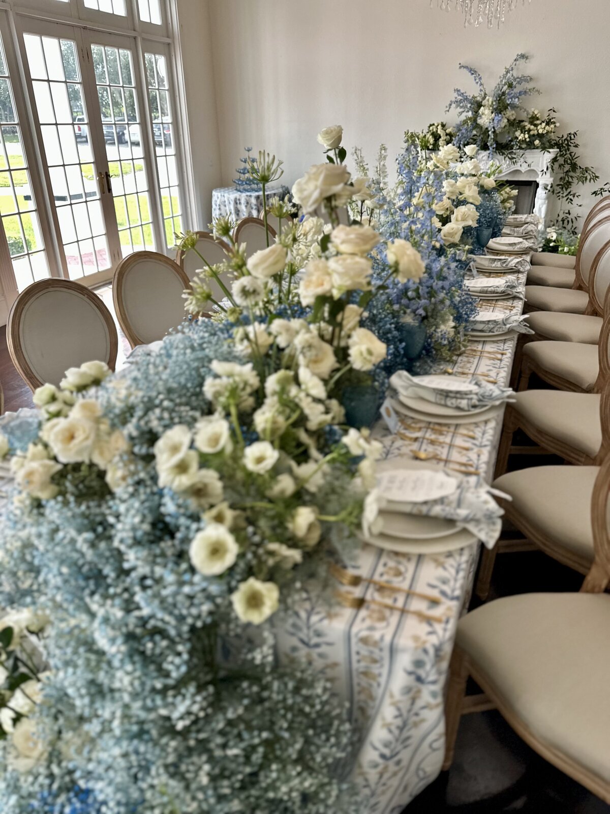 A breathtaking wedding tablescape featuring a luxurious blue floral runner cascading elegantly to the floor. The refined blend of lush florals, delicate table settings, and soft candlelight creates a sophisticated and romantic atmosphere, perfect for couples seeking a timeless wedding aesthetic.