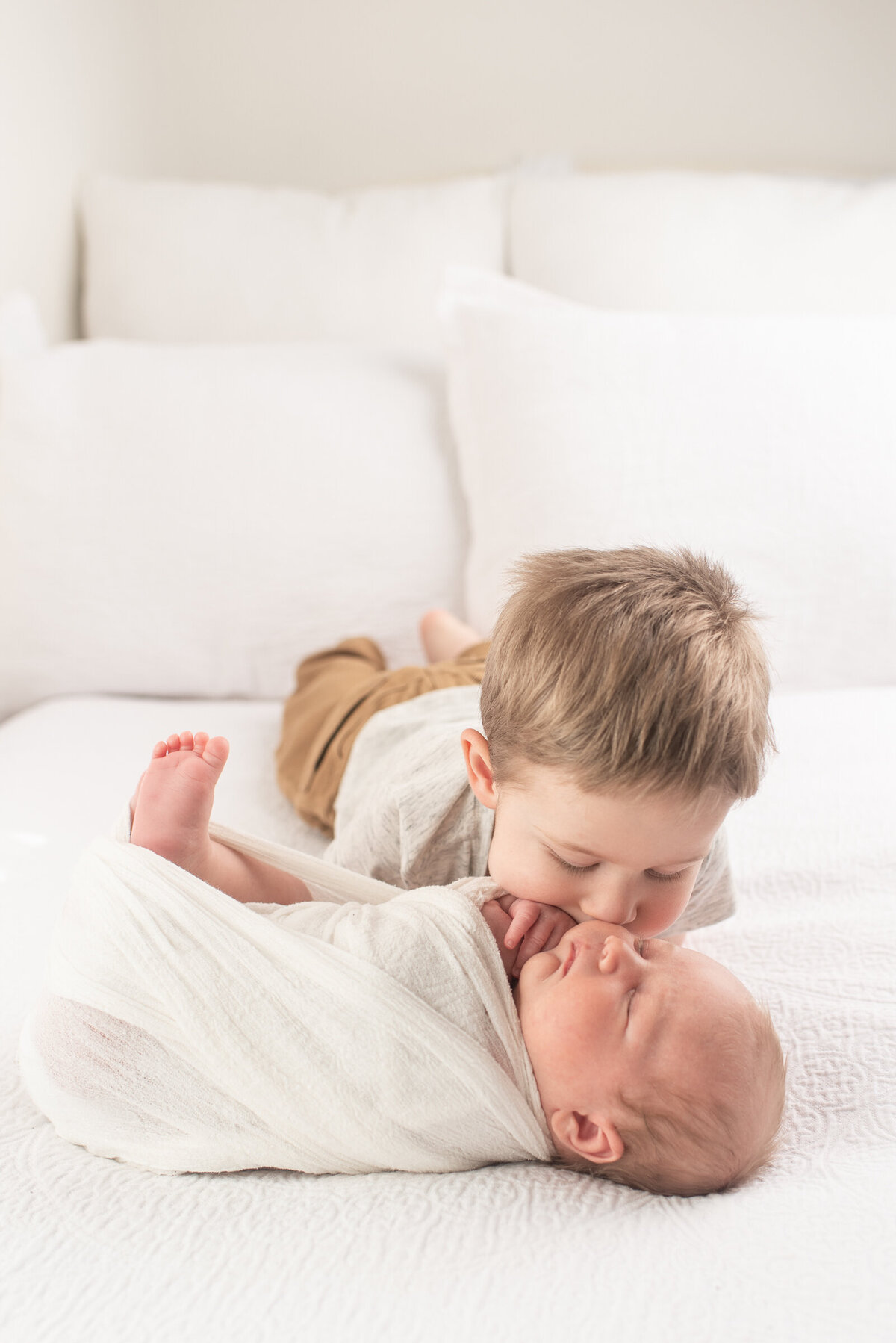Big brother kissing baby brother on white bed