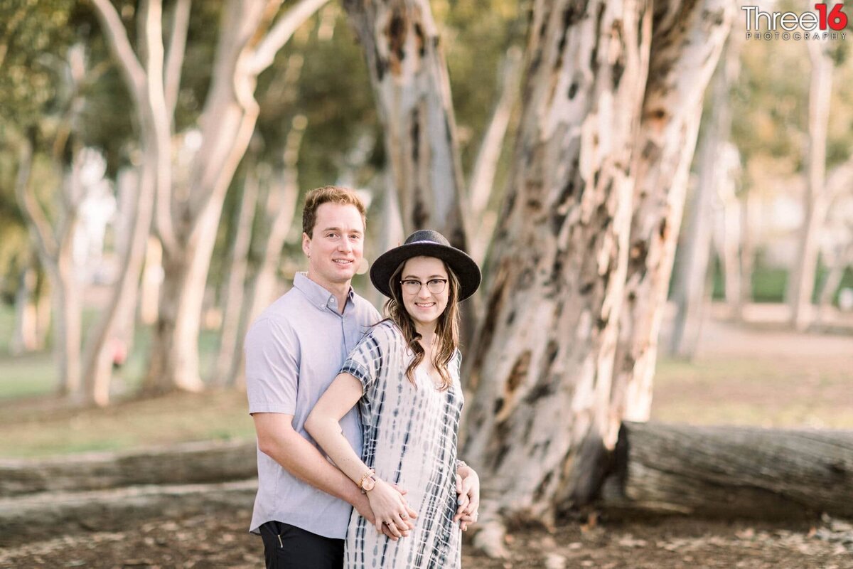 Engaged couple pose for photos with large tree behind them