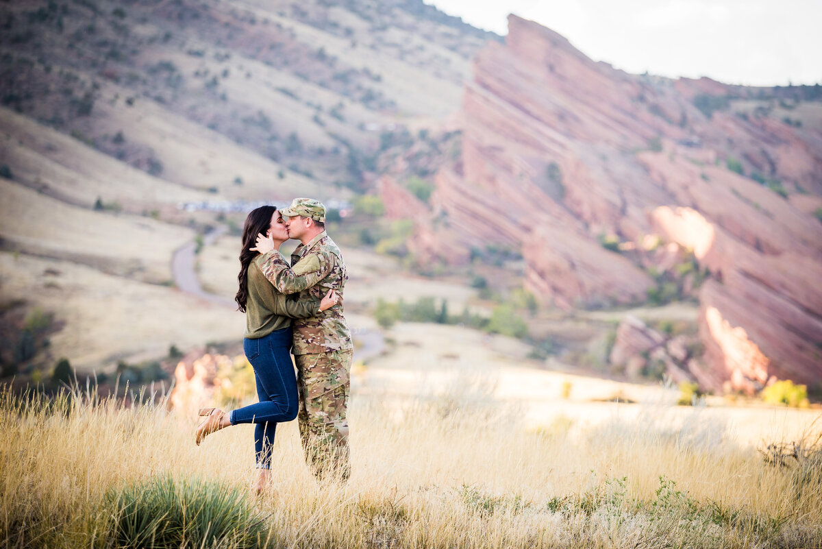 A man in a military uniform grabs his fiancée's face for a kiss and she pops a leg.