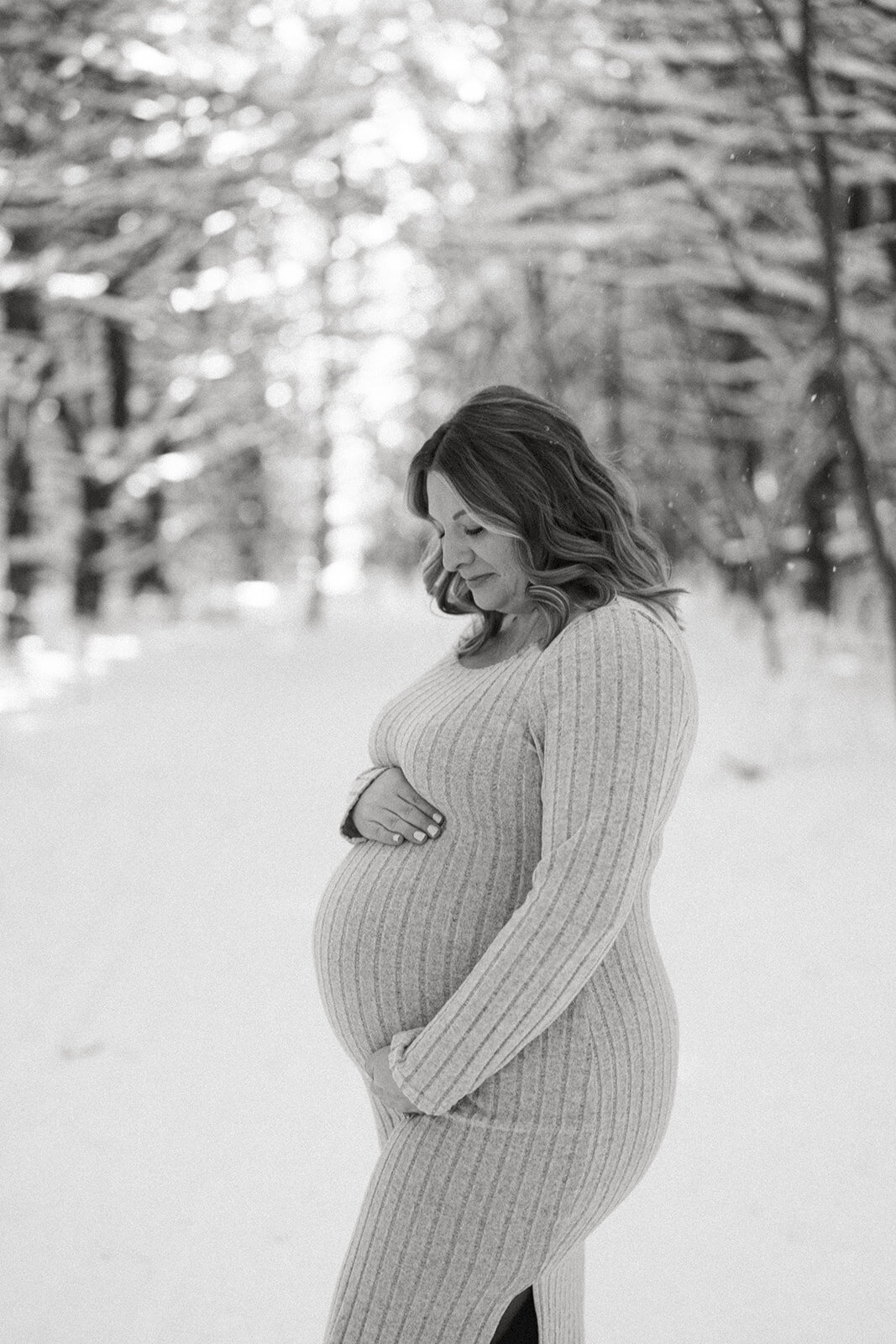 Black and white photo of a pregnant woman holding her belly during a winter maternity session at Al Sabo Preserve in Kalamazoo Michigan.