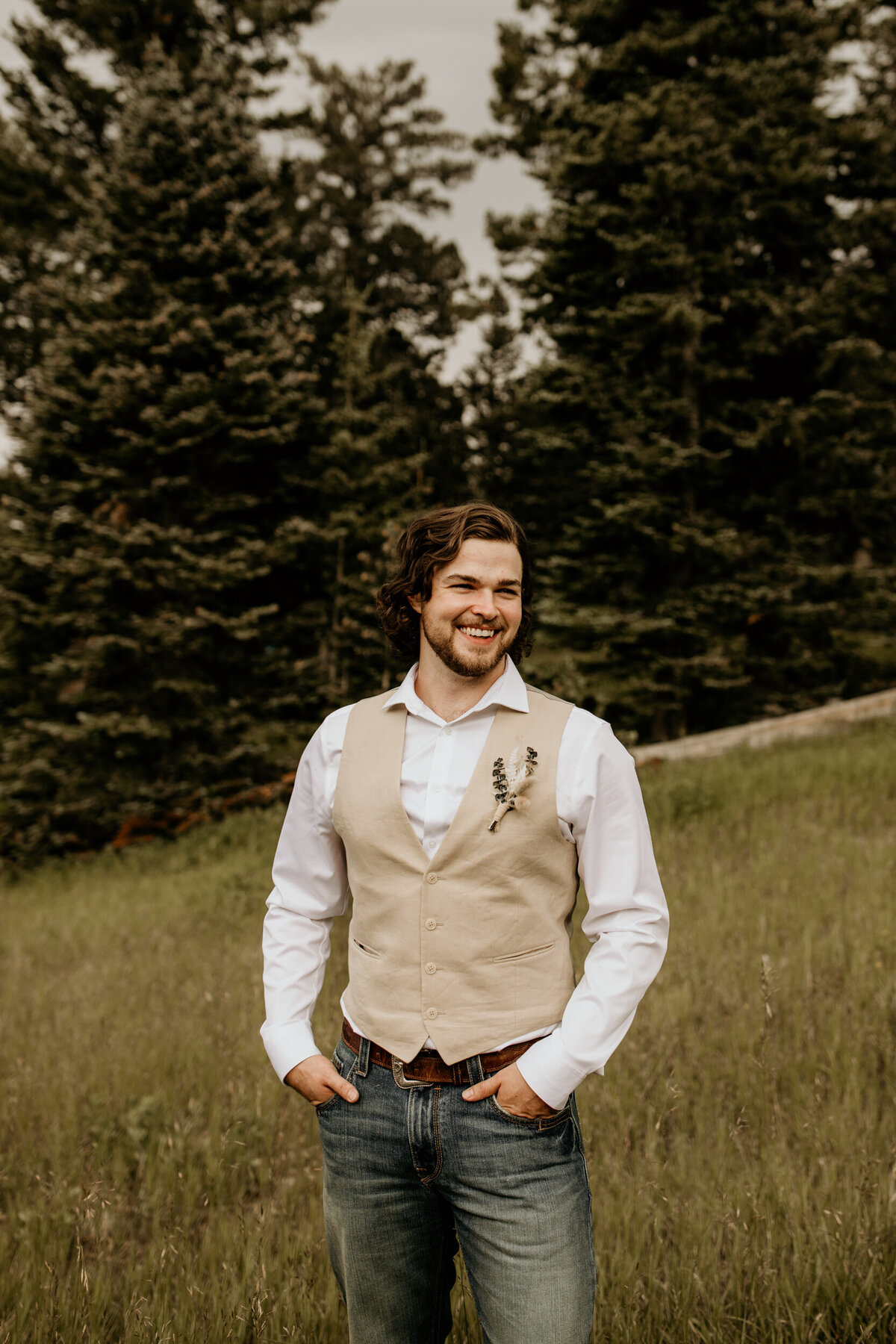 groom wearing a tan vest and jeans smiling in New Mexico