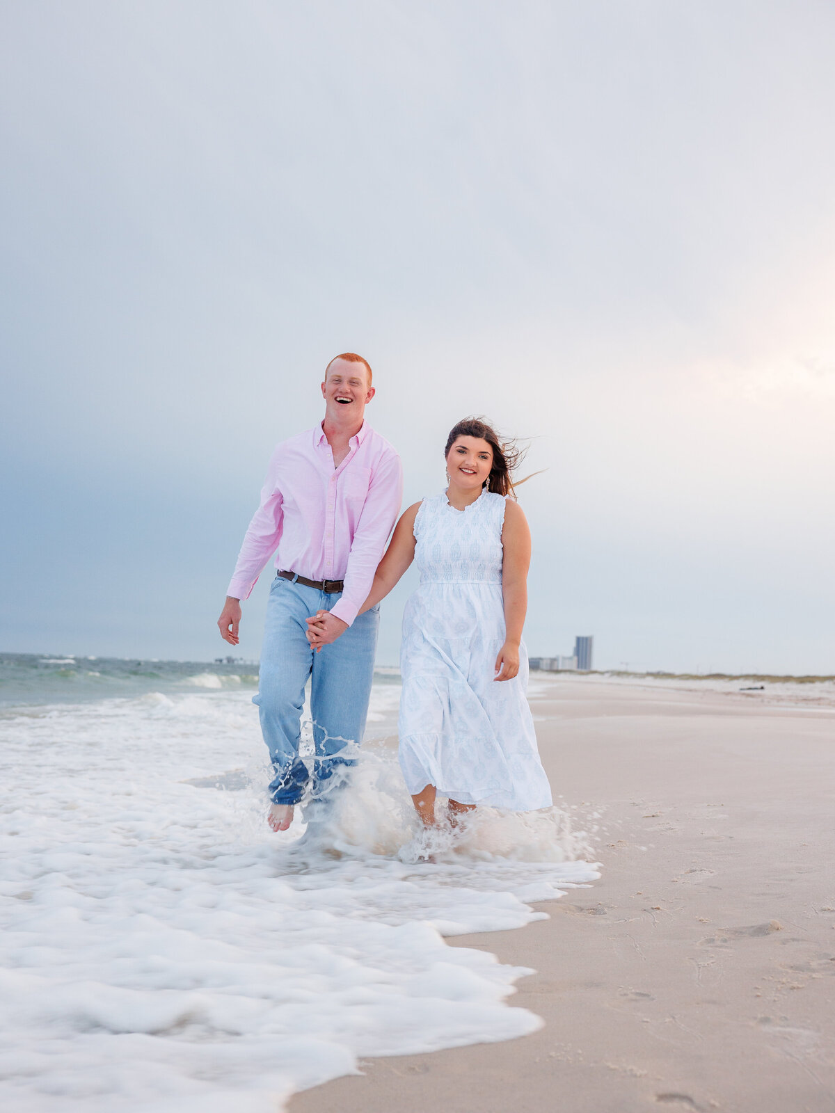 genuine laughter as couple walks on beach when waves crash at feet getting couple wet