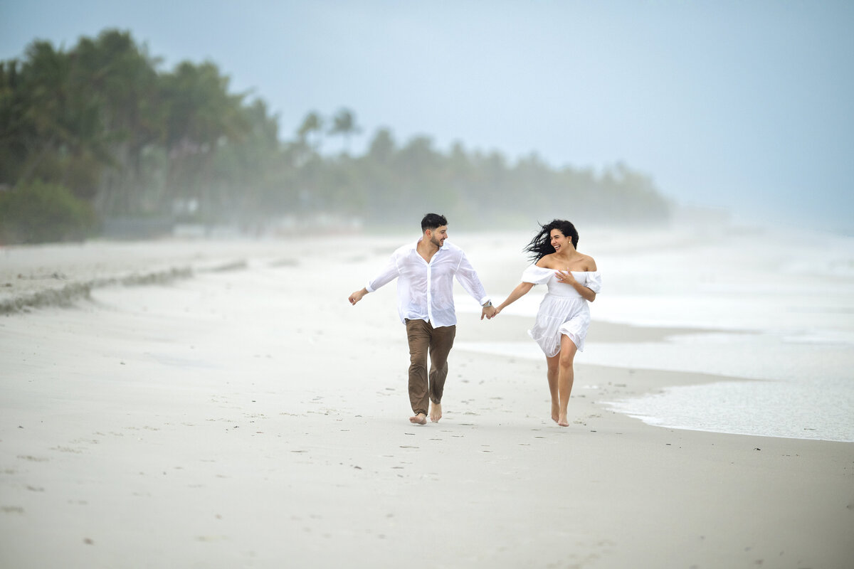Naples Florida couple holding hands and running in the rain just after she said yes