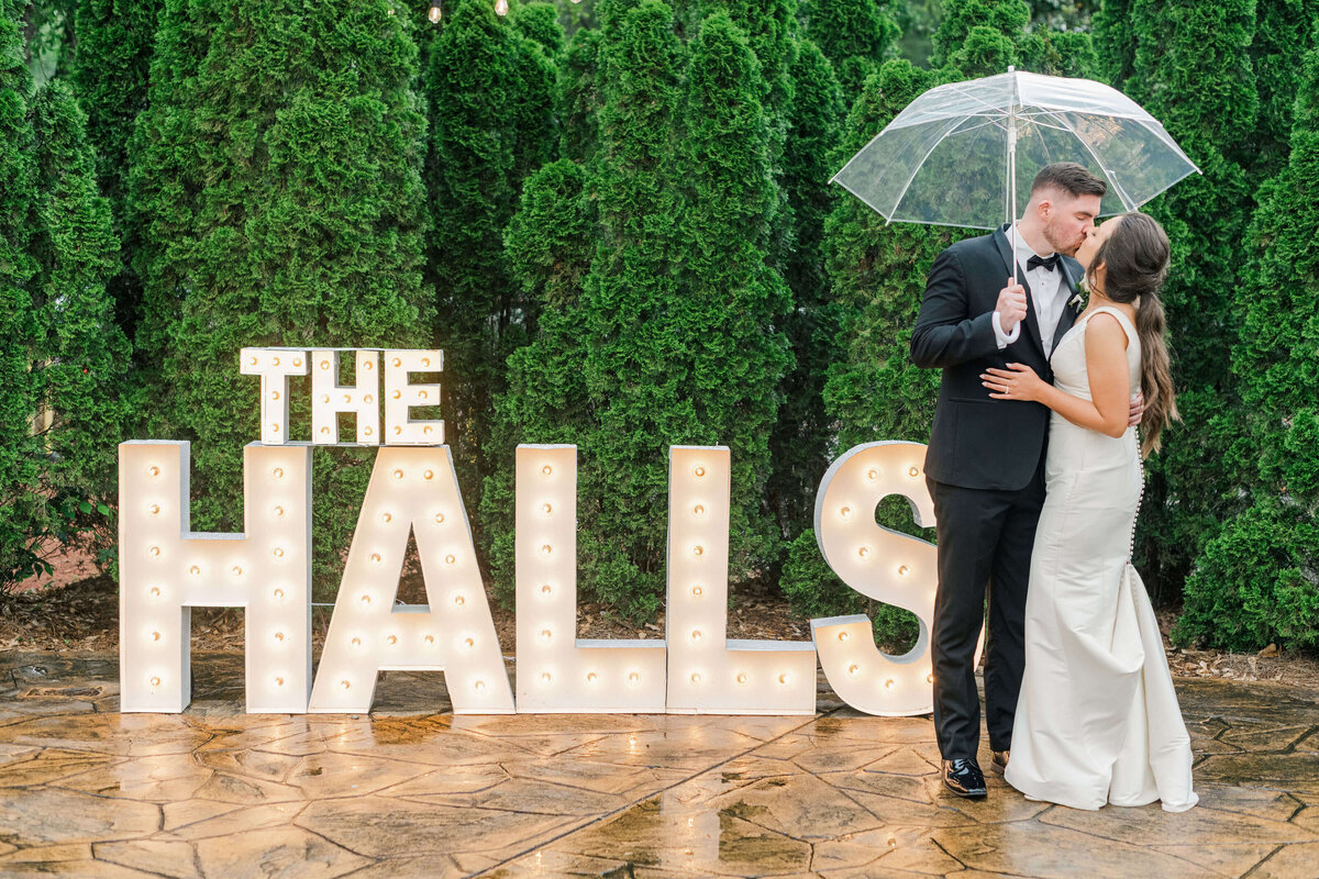 Bride and groom standing under umbrella with lightup large box letters of their last name