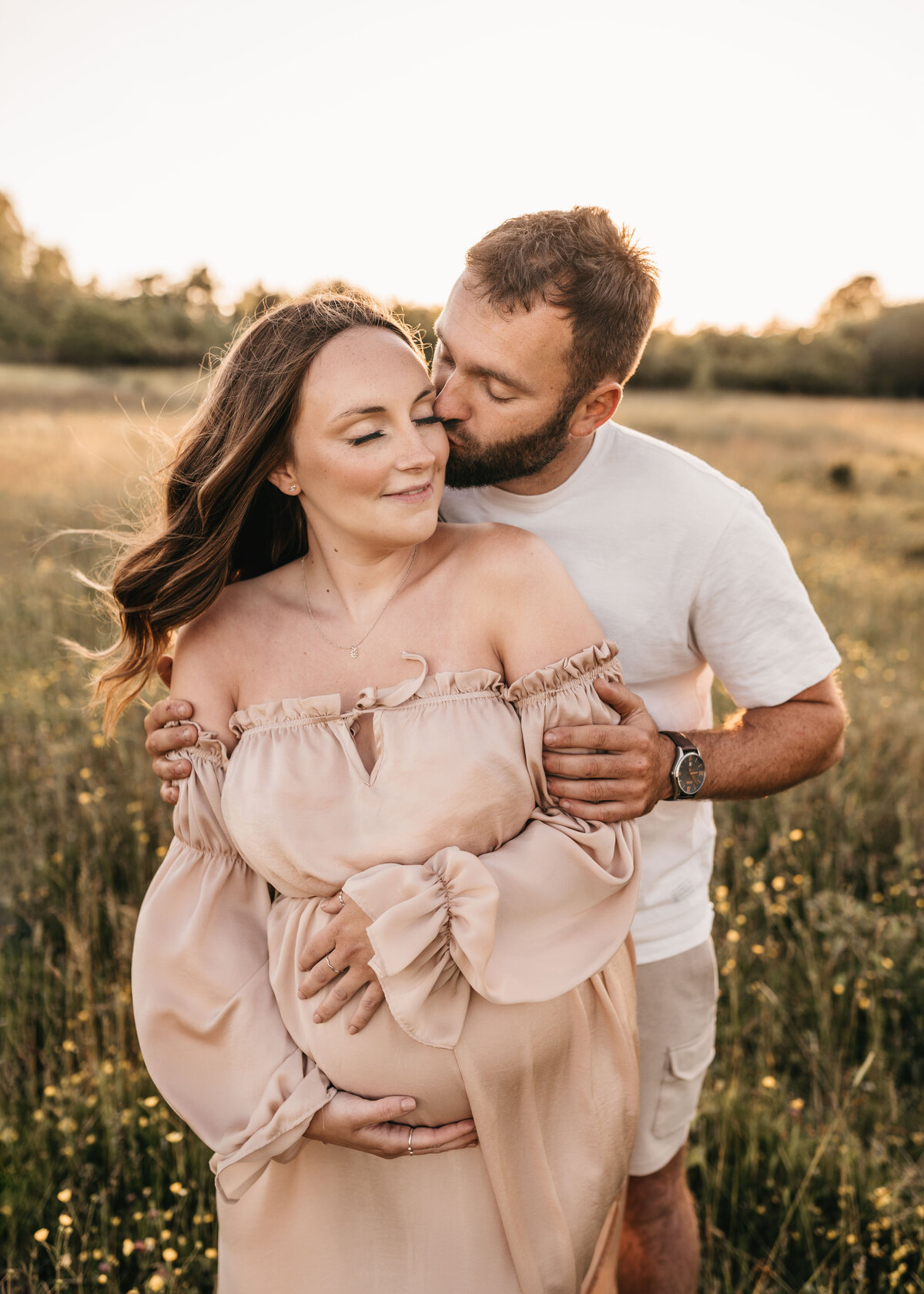 Photo of a couple having a maternity photoshoot outdoors at sunset in a field of flowers