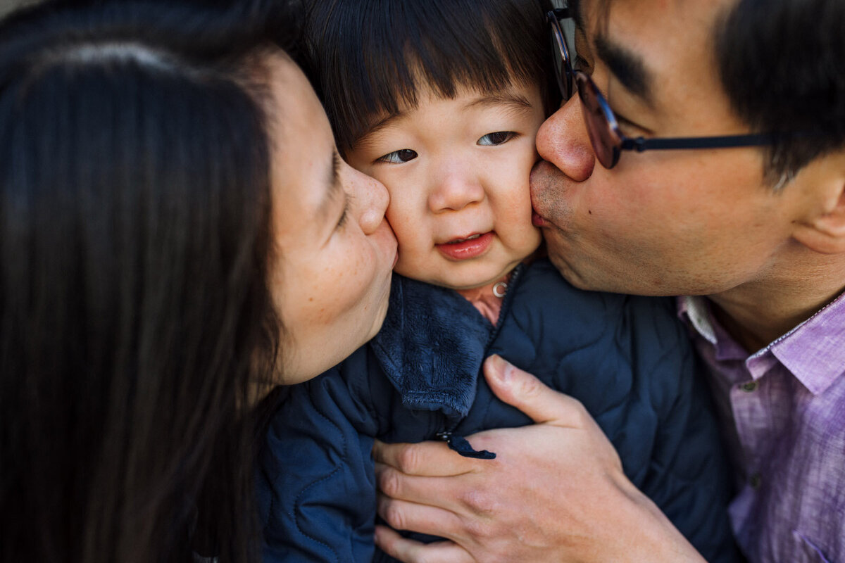 mom and dad kissing toddler son's cheeks at the same time