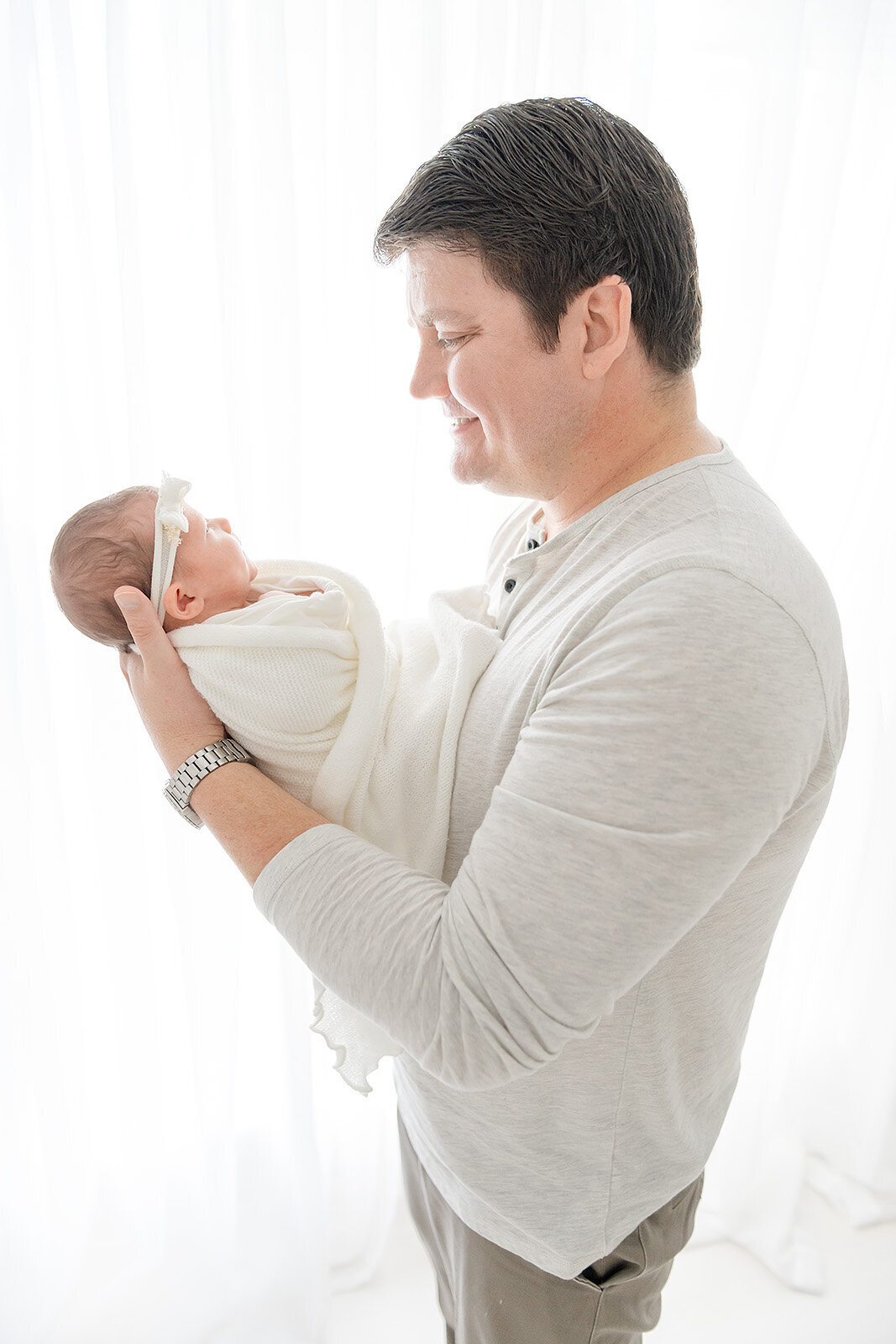 a father holding his baby in front of a white window