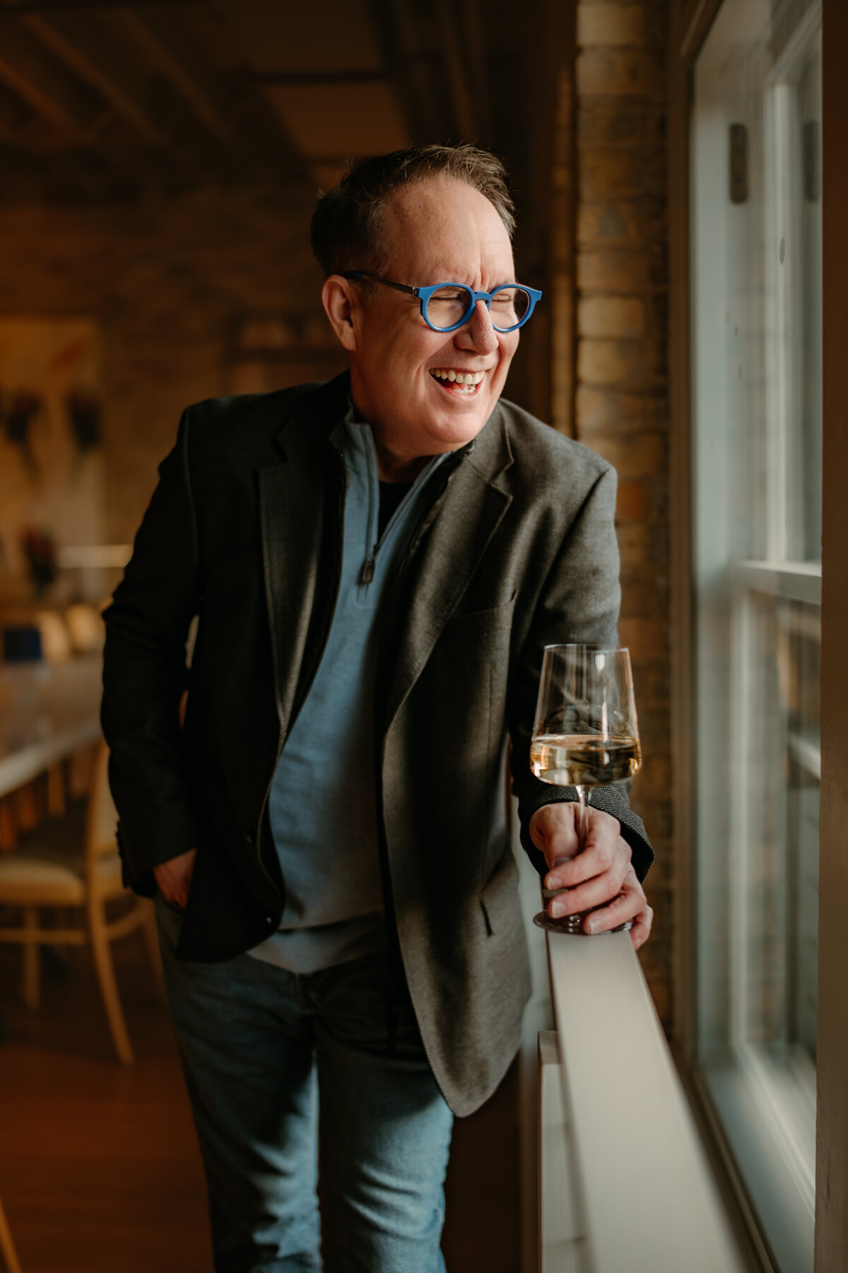 Minneapolis dating profile picture for dating apps. Man standing next to window laughing holding a glass of wine