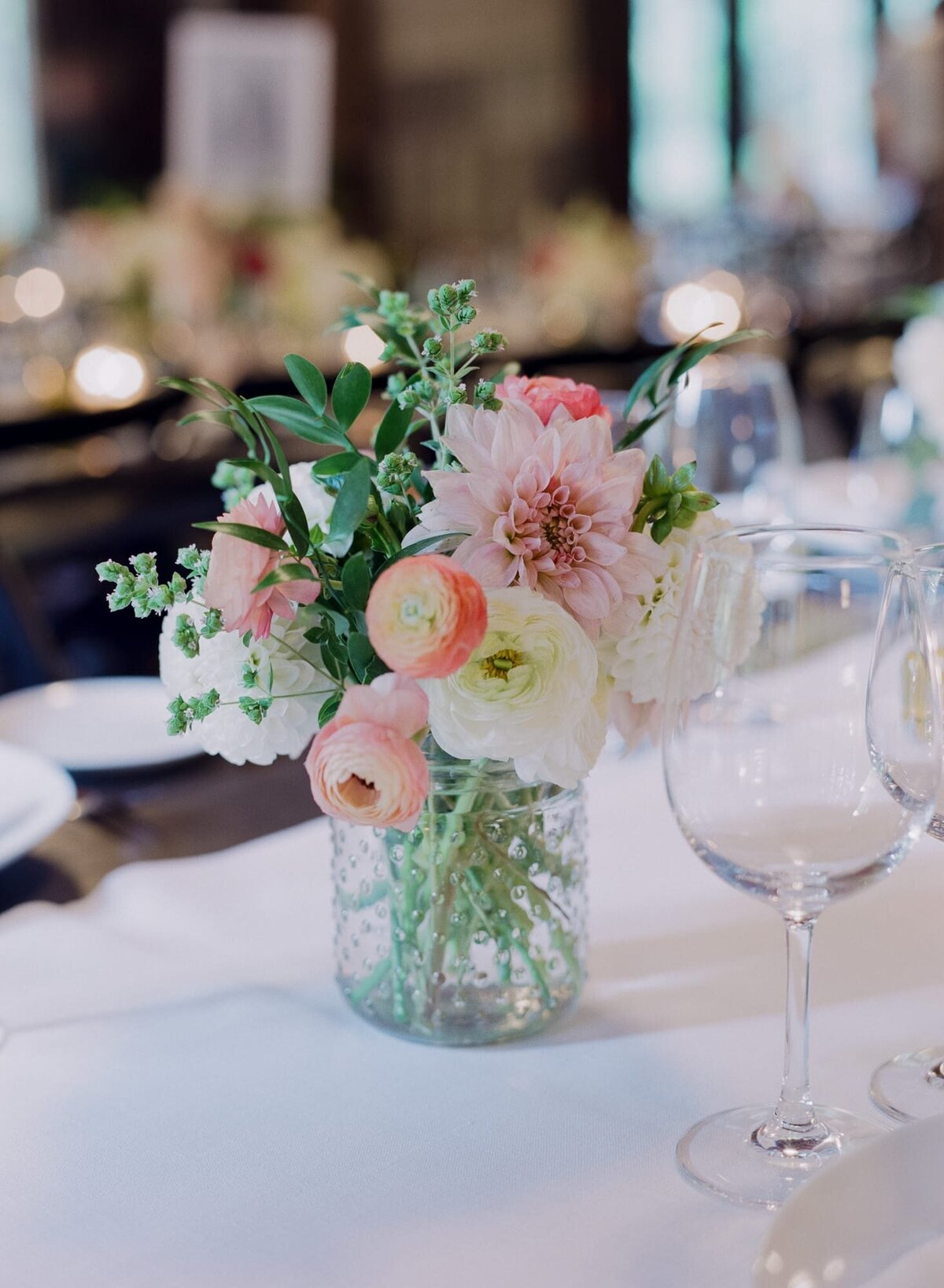 Beautiful floral arrangements of different flowers placed inside a transparent glass jar, alongside wine glasses.