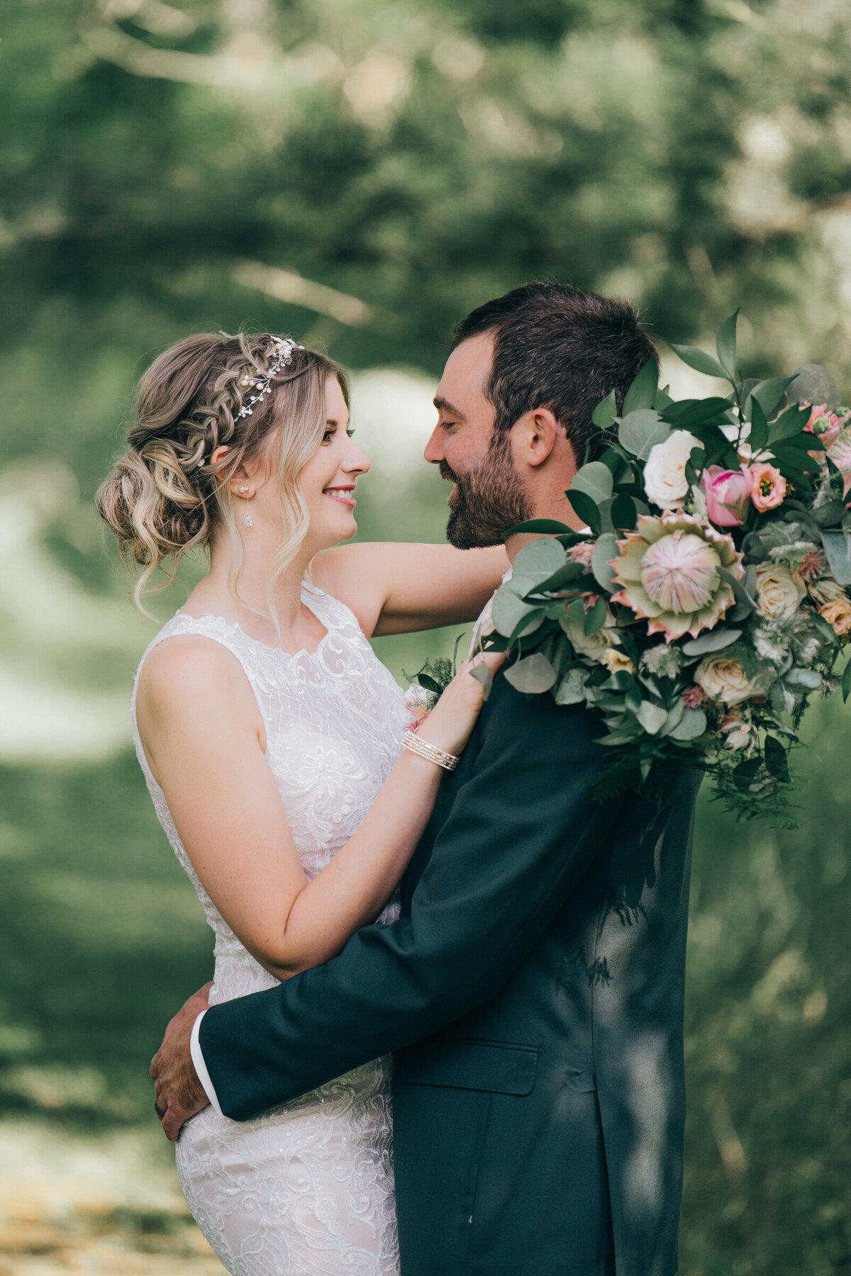 A bride wearing an elegant lace wedding dress smiling at her groom wearing a green wedding suit