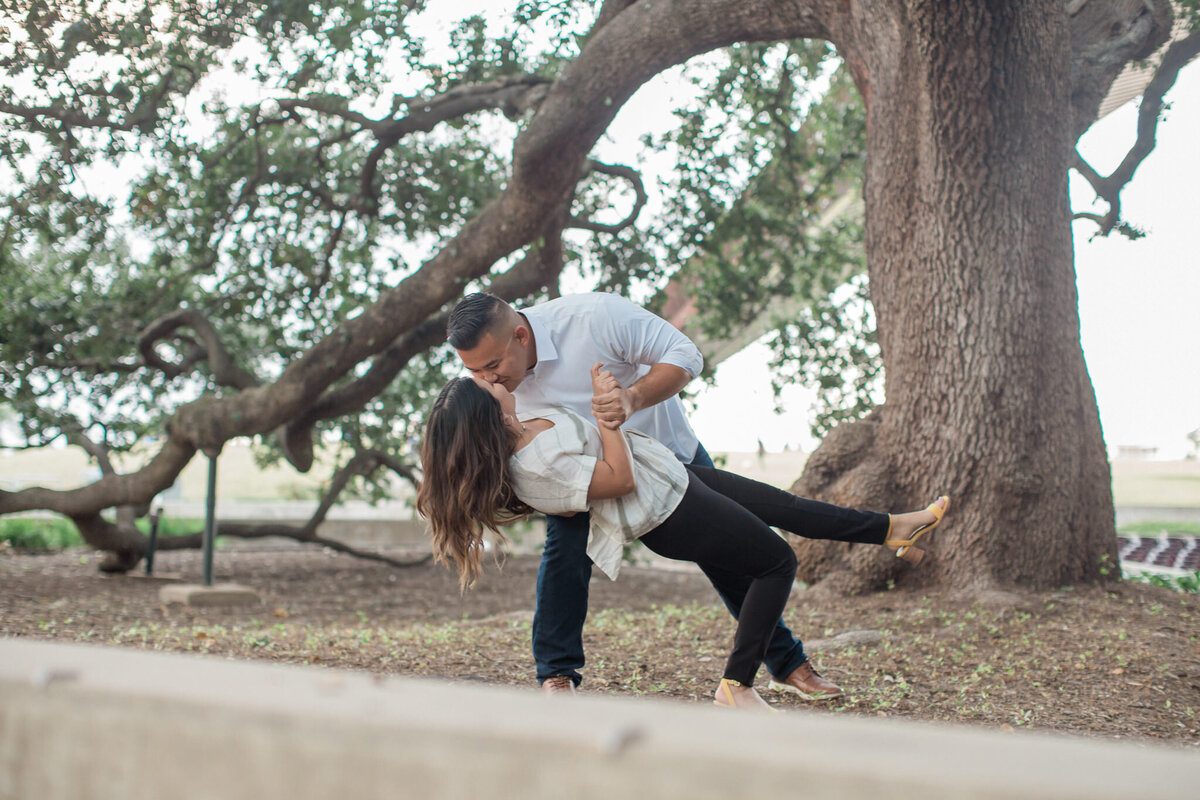 An affianced man leans in to kiss his betrothed bride to be under the oak trees