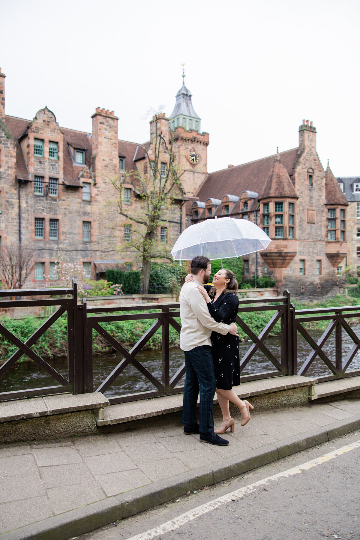 girl and boy snuggle under umbrella in Dean Village in Edinburgh, photo by Love is Magic Photo