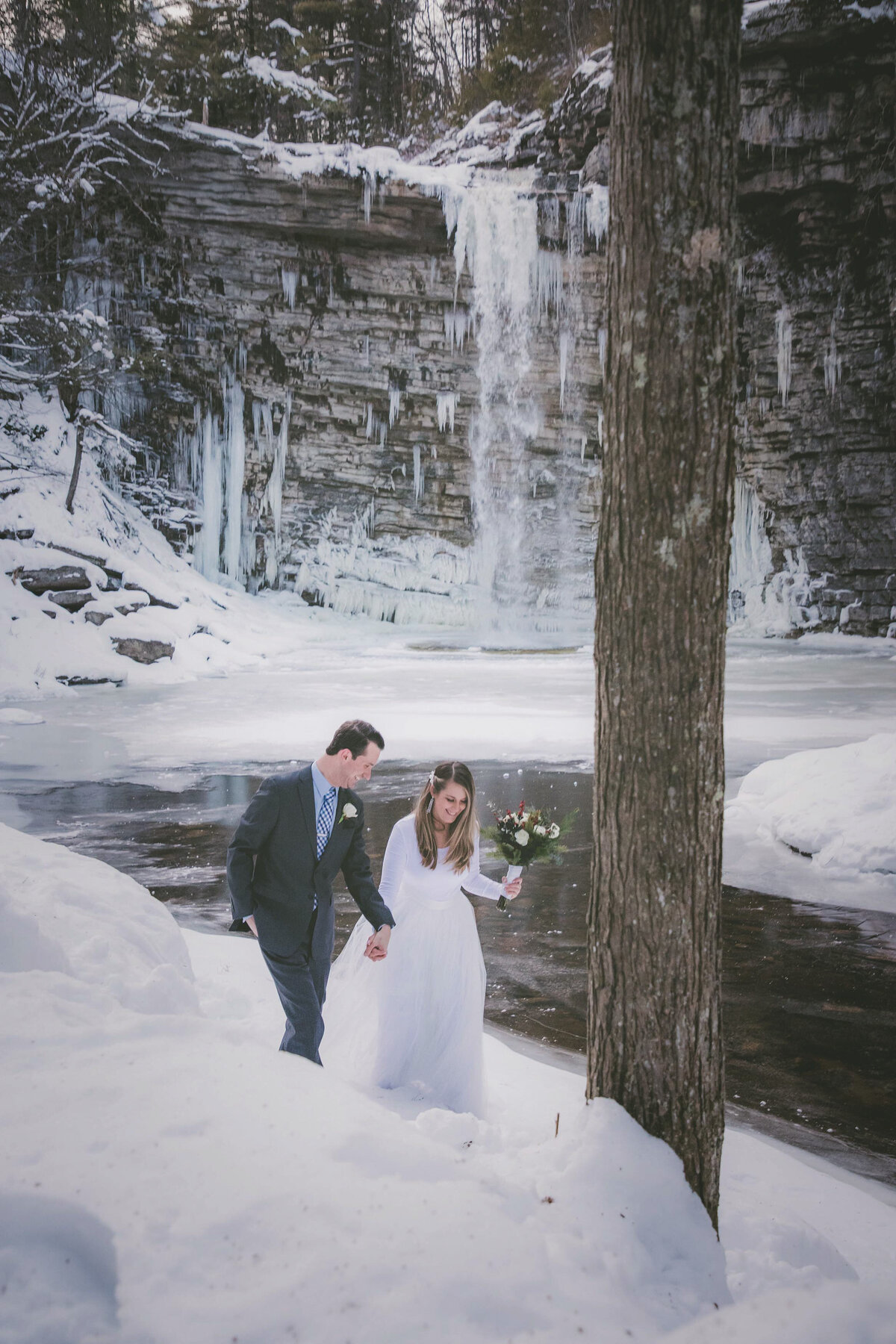 Nature view of frozen waterfall while couple walks in snow.