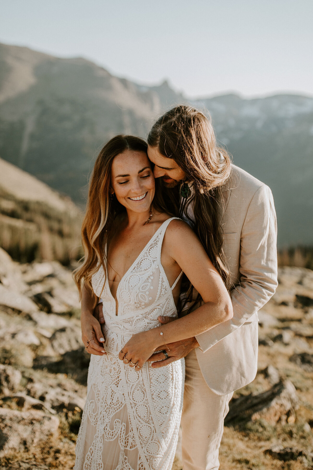 bride and groom wearing  an ivory wedding gown and suit pose side by side smiling in the mountains