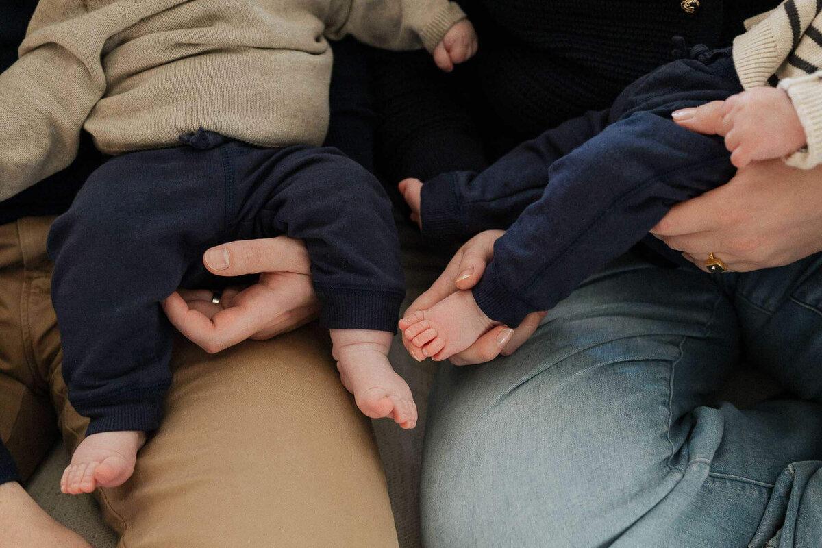 Close-up image of mom and dad  holding newborn baby boys. Cute toes and loving embrace during family photography session at home in Cleveland.