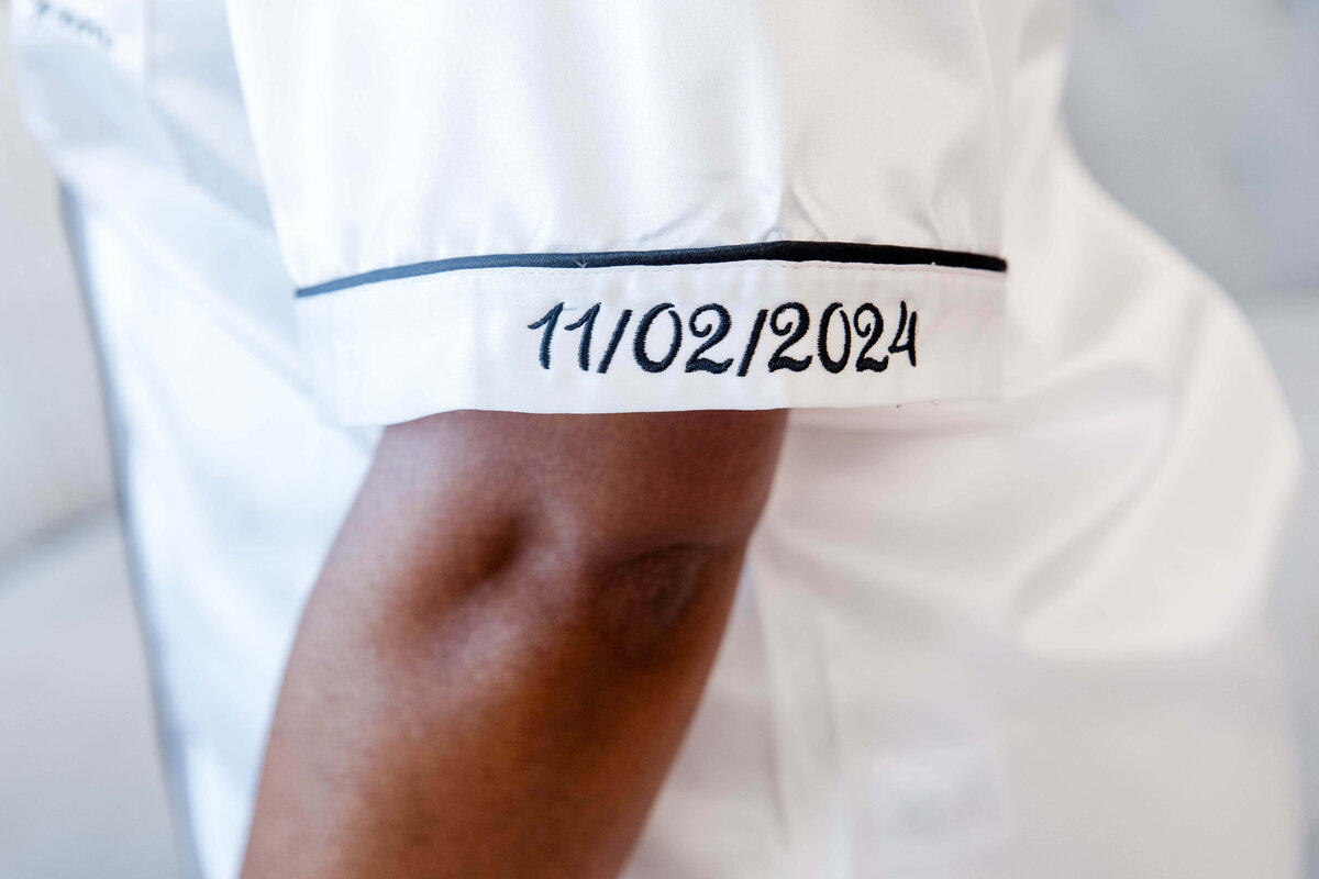 A close-up shot of the bride's satin pajama sleeve, elegantly embroidered with the wedding date "11/02/2023" in black thread.