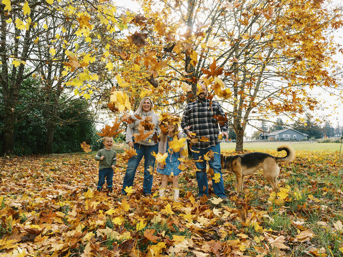 A family throwing leaves into the air during a family photo shoot by Among the Oaks.