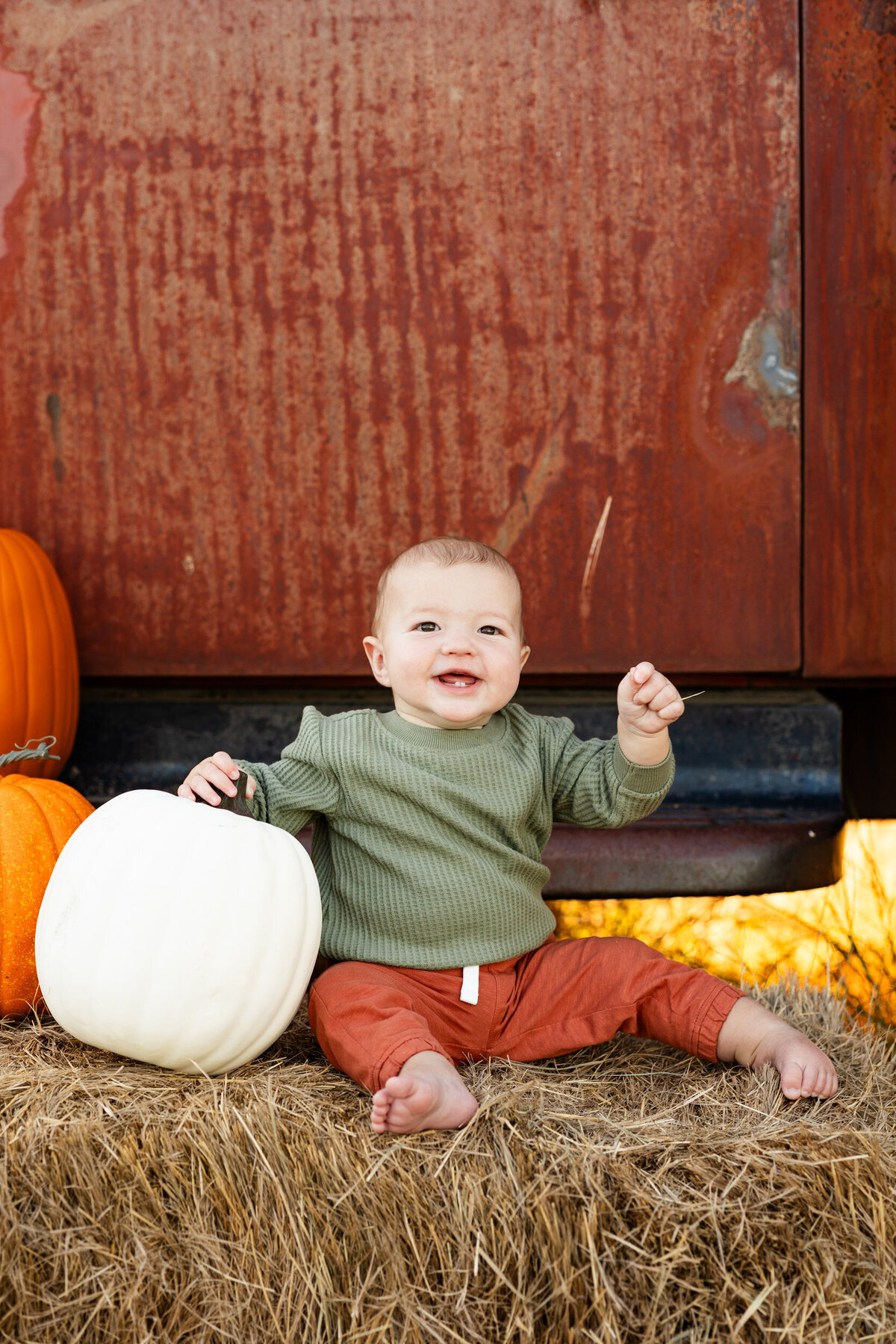 Baby boy holds stem of white pumpkin and smiles.