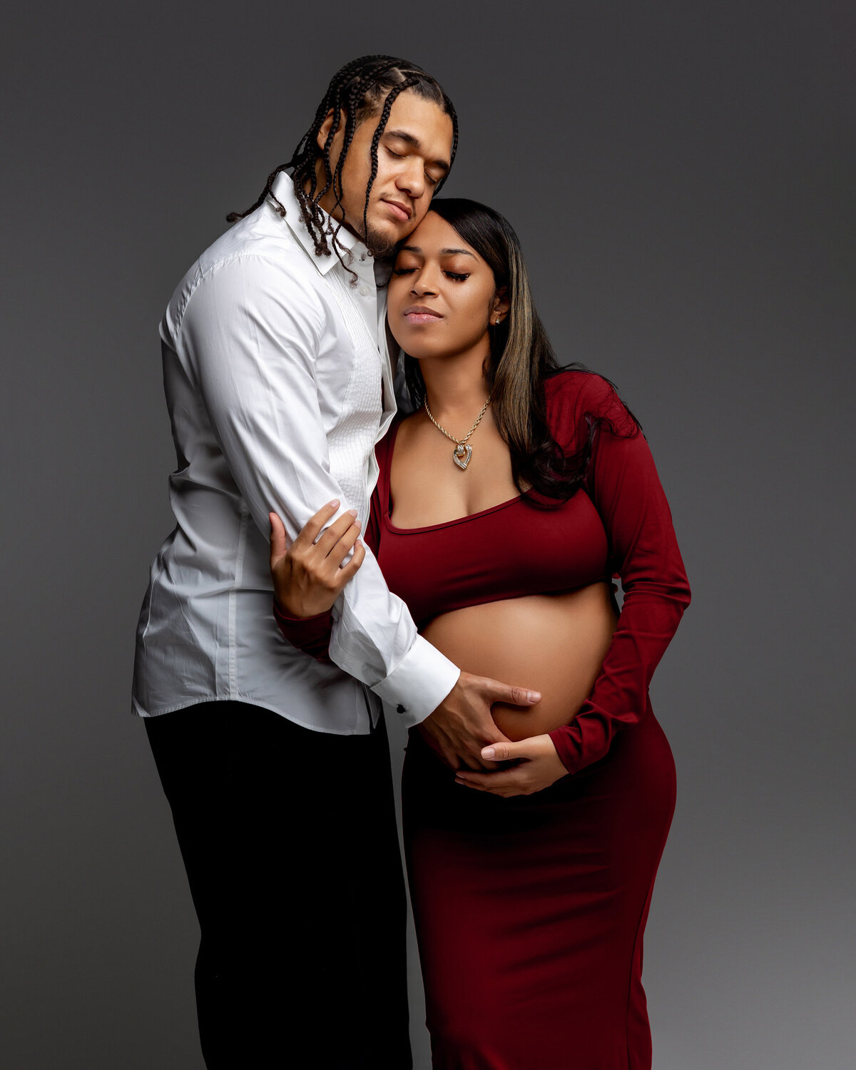 Mama-to-be in a red dress, she and her husband embrace each other, sharing a tender moment filled with love and anticipation for their growing family. Captured by Inland Empire photographer Kaitlyn Dawn Photography.