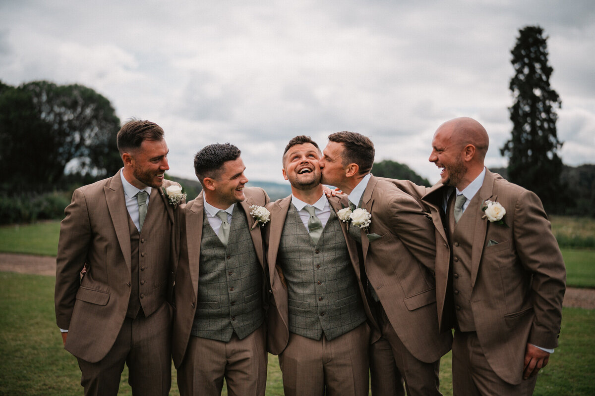 Groom and groomsmen laughing and joking together in matching suits at Broadfield Court farm wedding venue in Herefordshire.