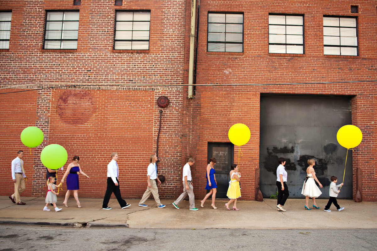 A wedding party march down the street with large balloons.