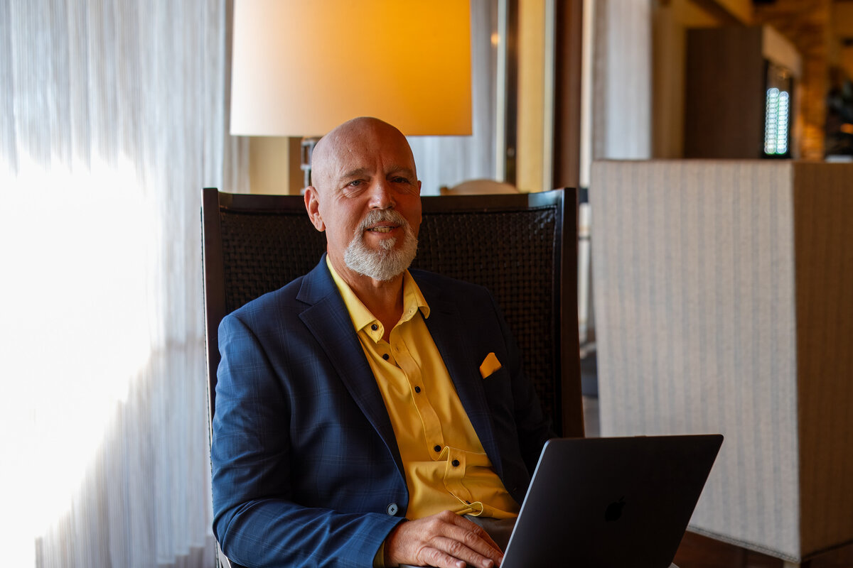 Man smiling while working on a laptop in a warmly lit indoor setting, photographed by Vyrl Photo, showcasing Tucson brand photography.