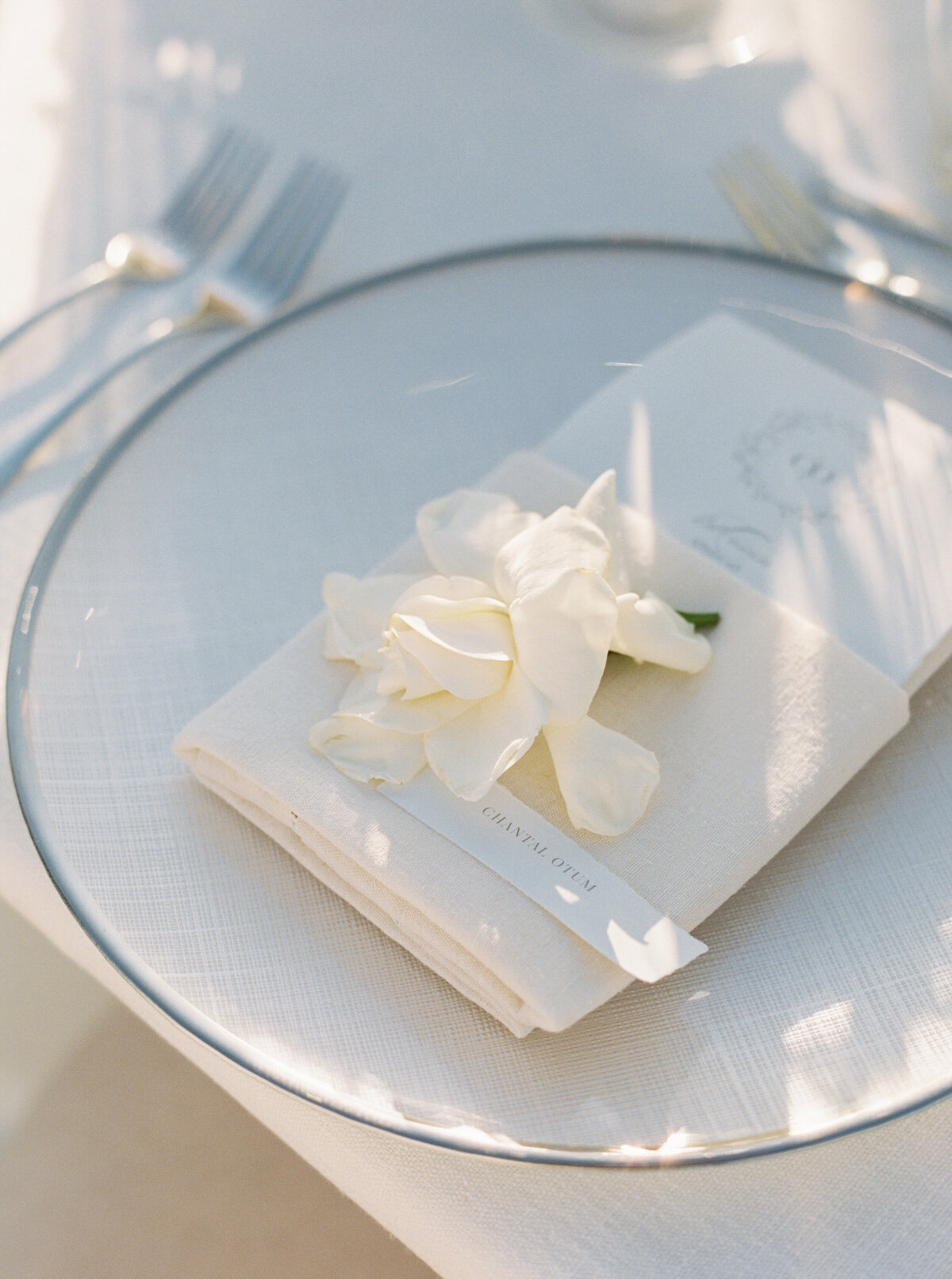 simple, white and silver place setting using single gardenia bud from max gill design and white and silver charger from hensley event rentals.