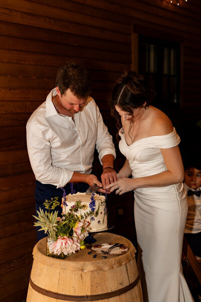 A bride hugs a man, both smiling warmly, during an outdoor wedding ceremony captured by a New England Wedding Photographer. She wears a long white dress and veil. In the background, guests in formal attire stand near trees and a wooden arch draped in foliage.