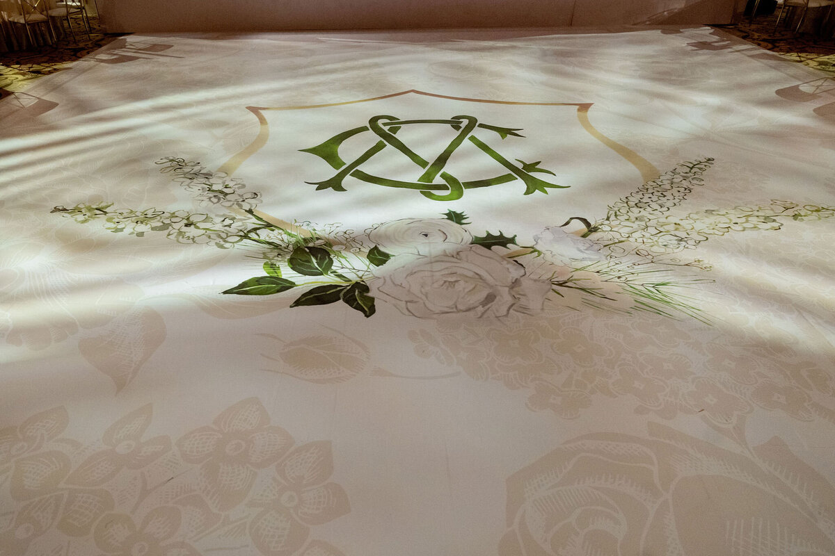 Custom wedding monogram projected onto the dance floor, surrounded by elegant floral decorations.