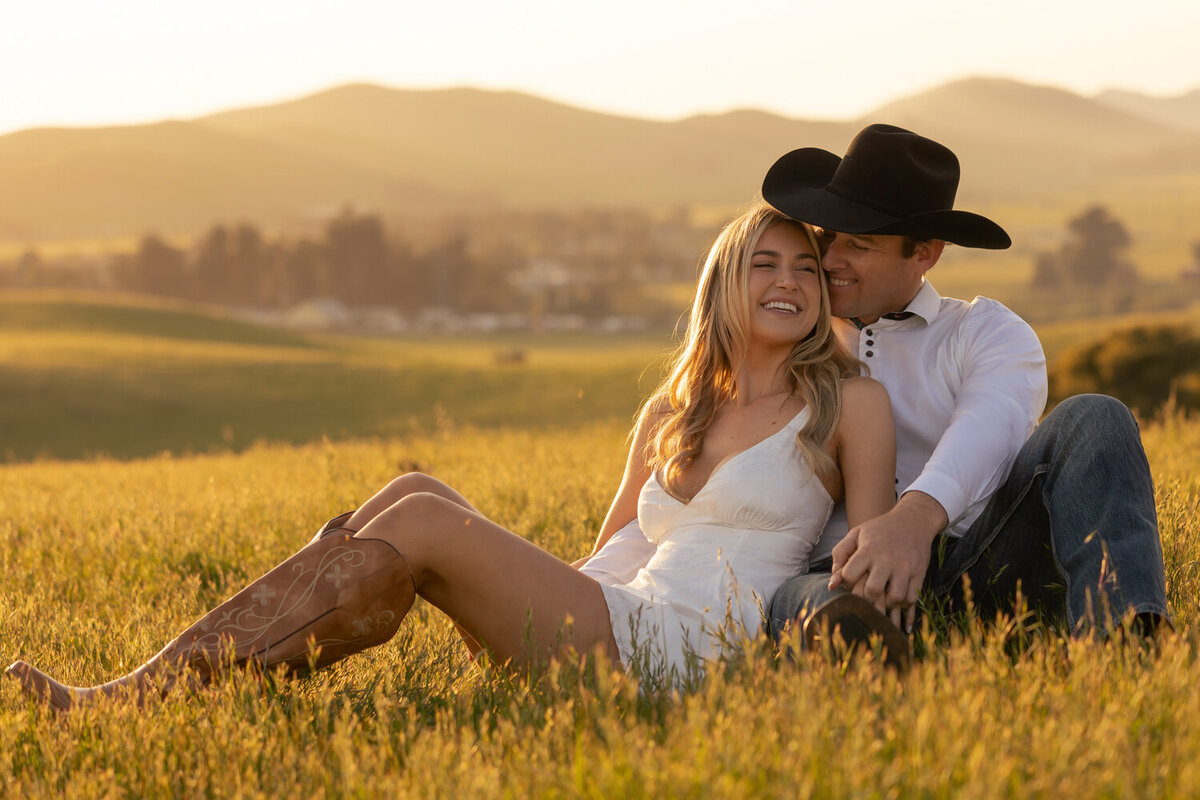 Candid couple laying in golden hour field with hills during engagement photos San Luis Obispo 
