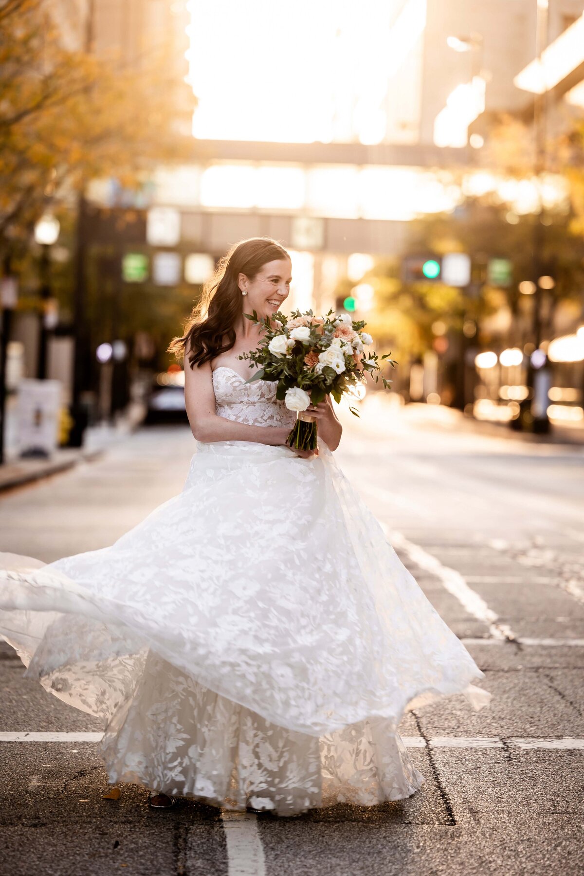 Embrace the joyous spirit of a bride dancing through the sunset-lit streets of Cincinnati in this captivating bridal portrait. As the city basks in the golden hour glow, this image captures the exhilarating moment of a bride celebrating her wedding day with spontaneous street dancing. This photo not only showcases her stunning gown and blissful smile but also embodies the vibrant energy of Cincinnati, making it an ideal inspiration for couples planning a lively urban wedding. Perfect for those who dream of a wedding day filled with fun and city charm.