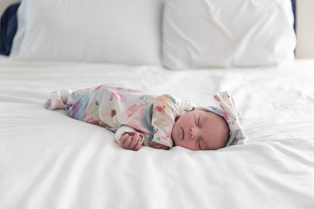 Newborn Baby in a Floral Romper Sleeping on Bed with White Covers