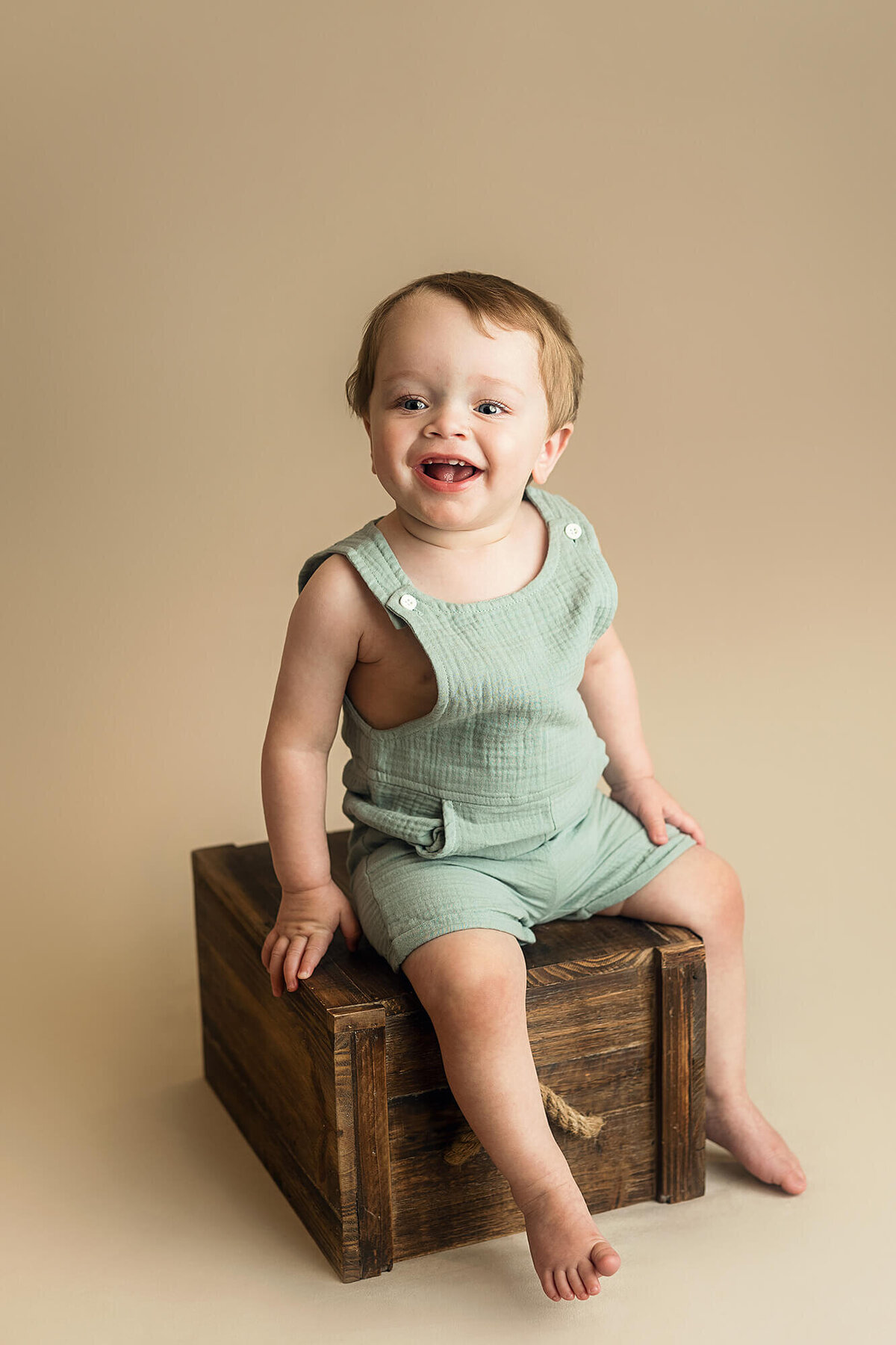 One year old boy sits on top of a wooden crate during his studio photo session.