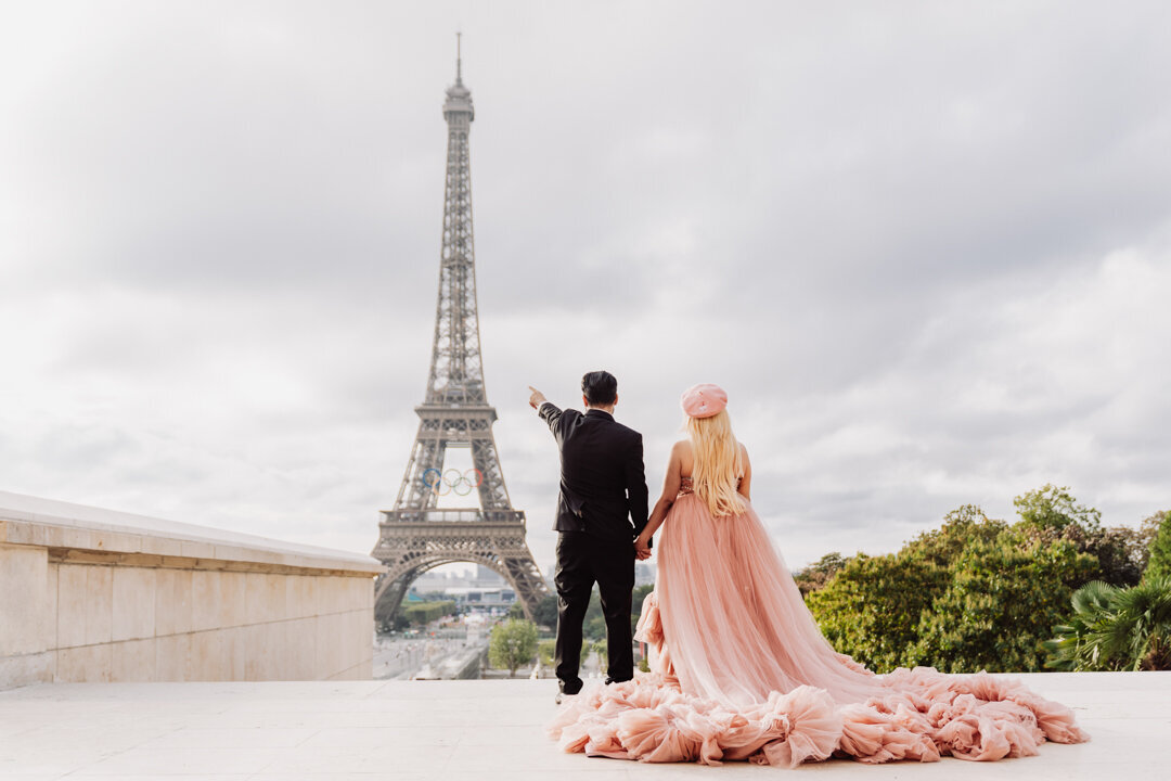 Romantic couple pose Paris, back view pointing at Eiffel Tower, pink princess dress, intimate moment capture