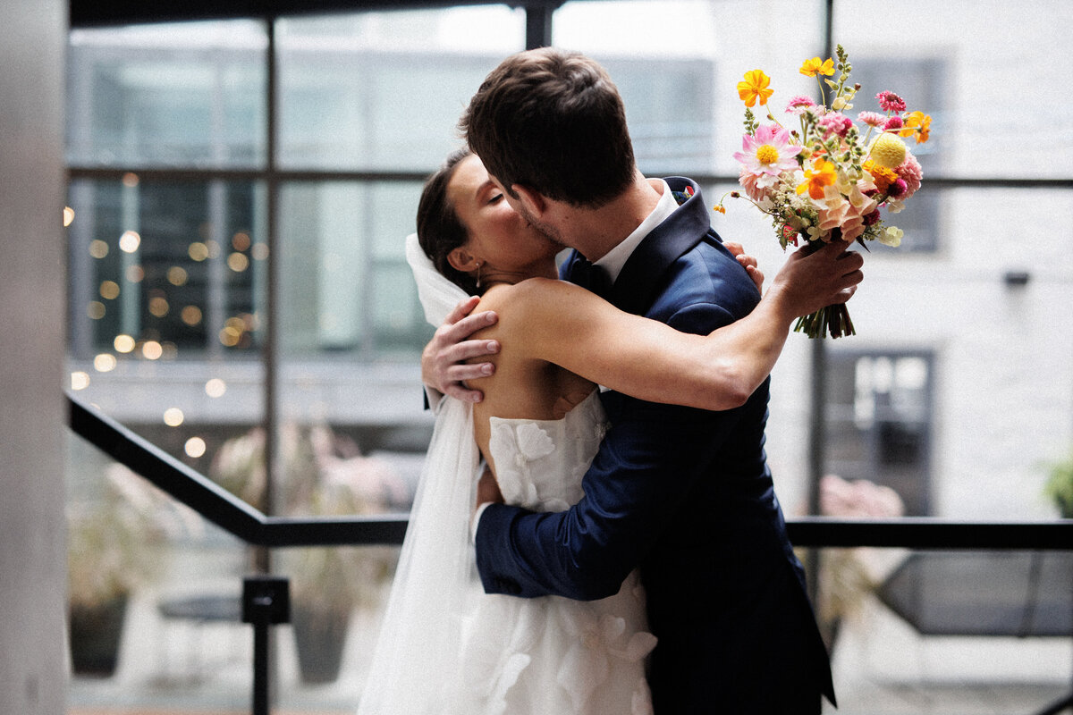 A bride and groom embrace at the Science Centre, the bride holding a colourful bouquet.